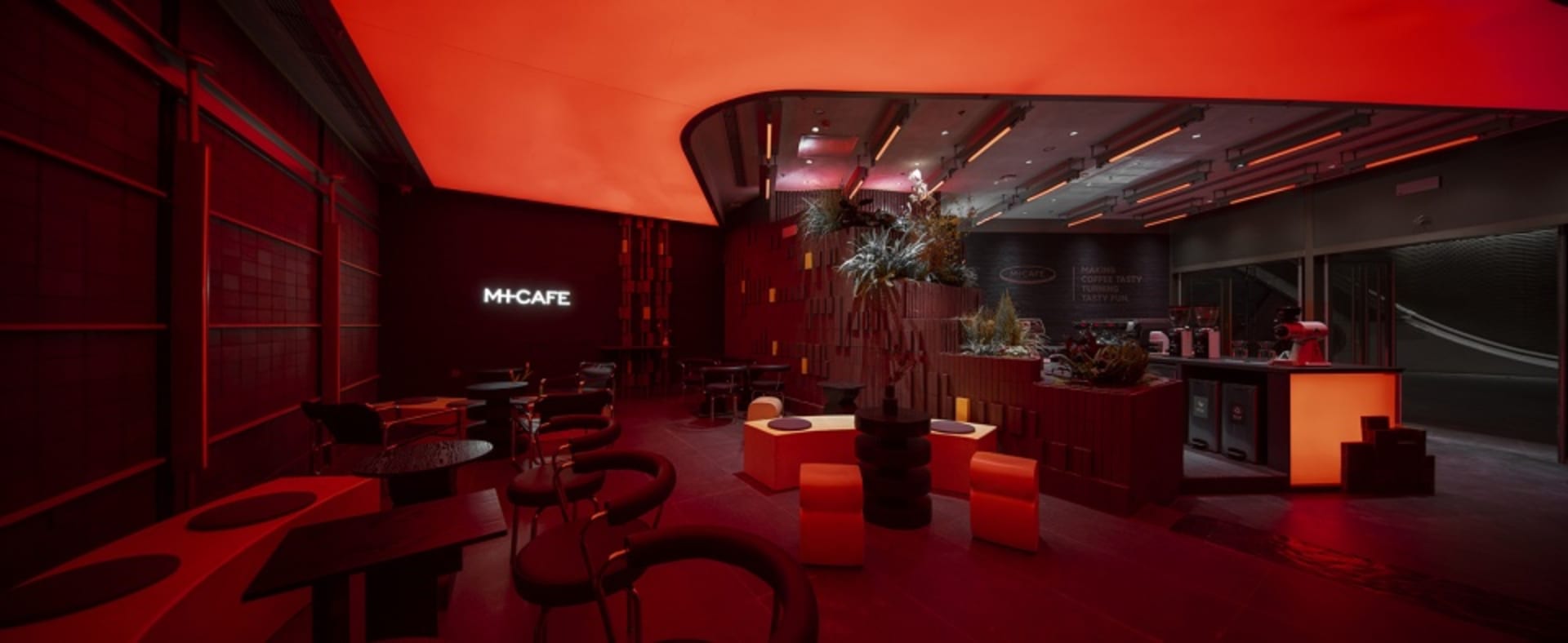 Warm and inviting cafe interior with red walls, orange accents, chairs, tables, and a potted plant