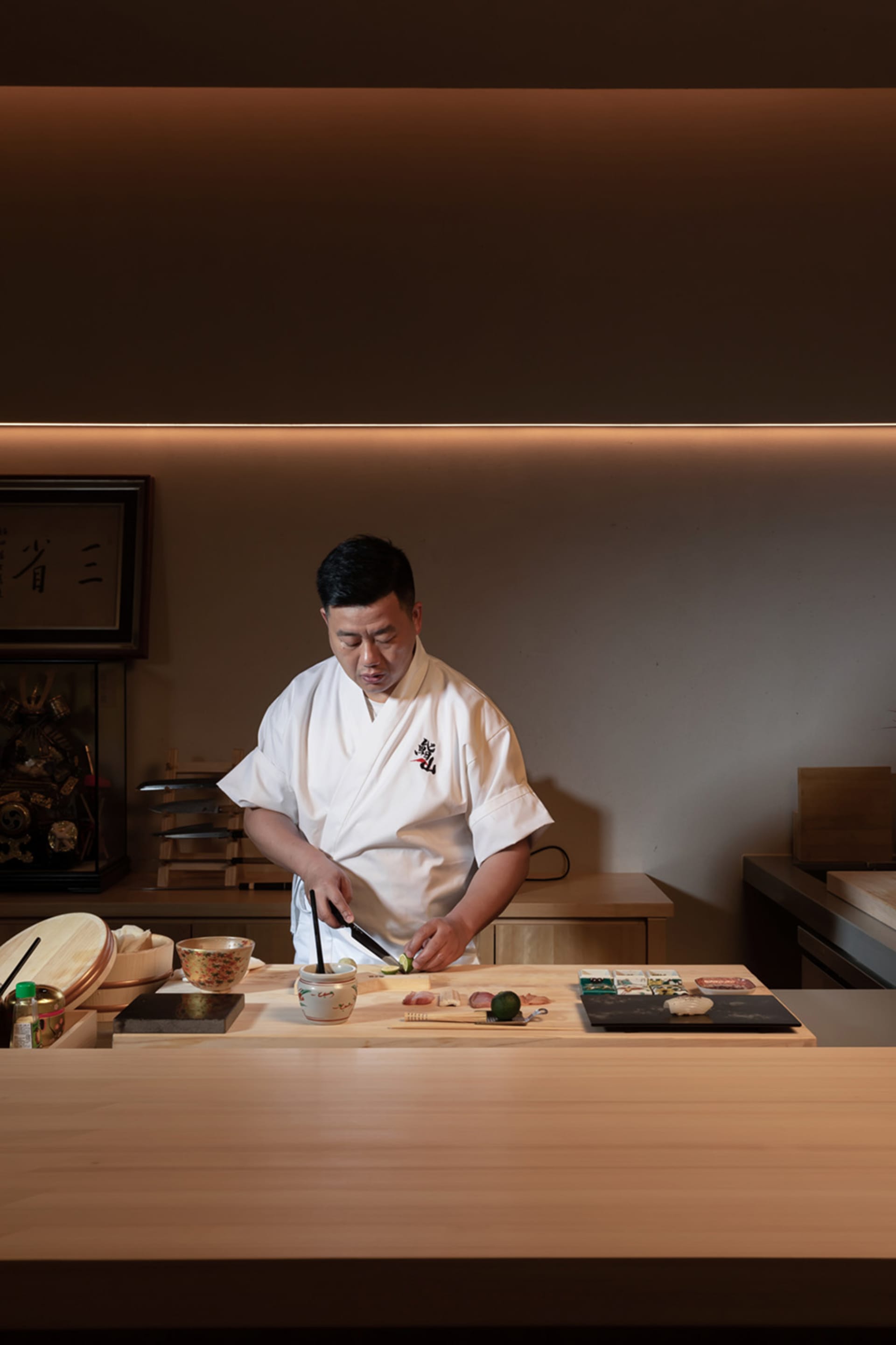 A man prepares food in a warm and inviting Asian-style kitchen with a wooden countertop, various kitchen items, and bottles