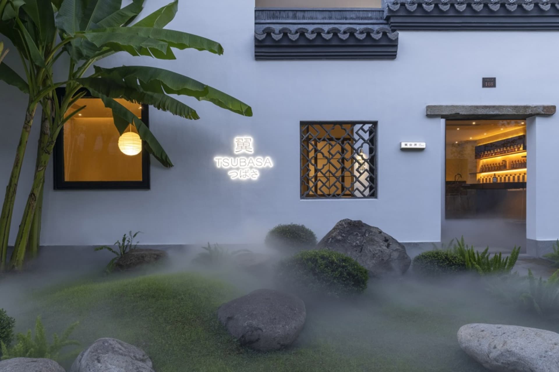 Asian-style house with a white exterior, green roof, and a large rock garden in front, blending traditional and modern elements in a serene and inviting atmosphere