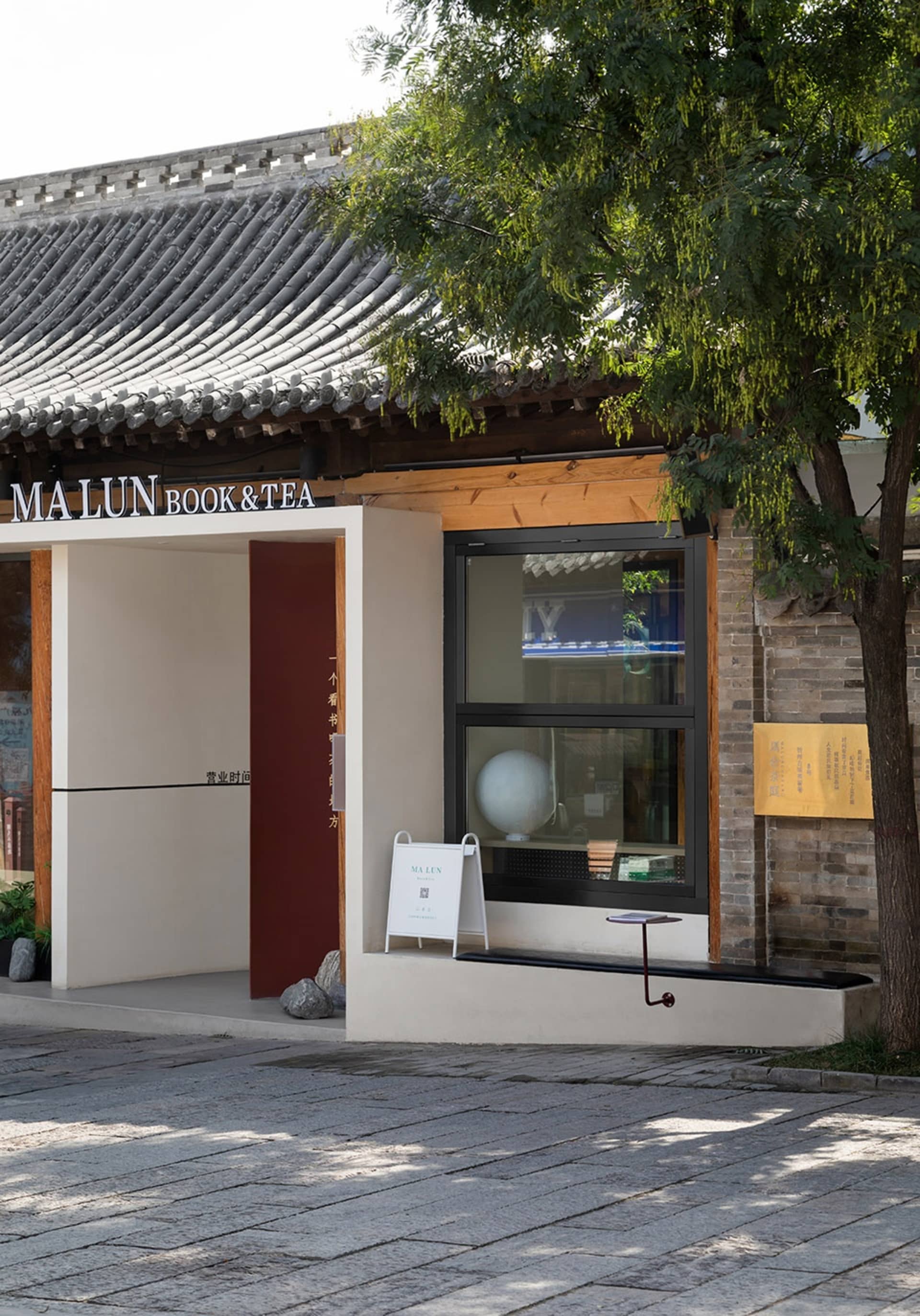 Asian-style house with a red door and a white wall, surrounded by two trees and a window with a sign