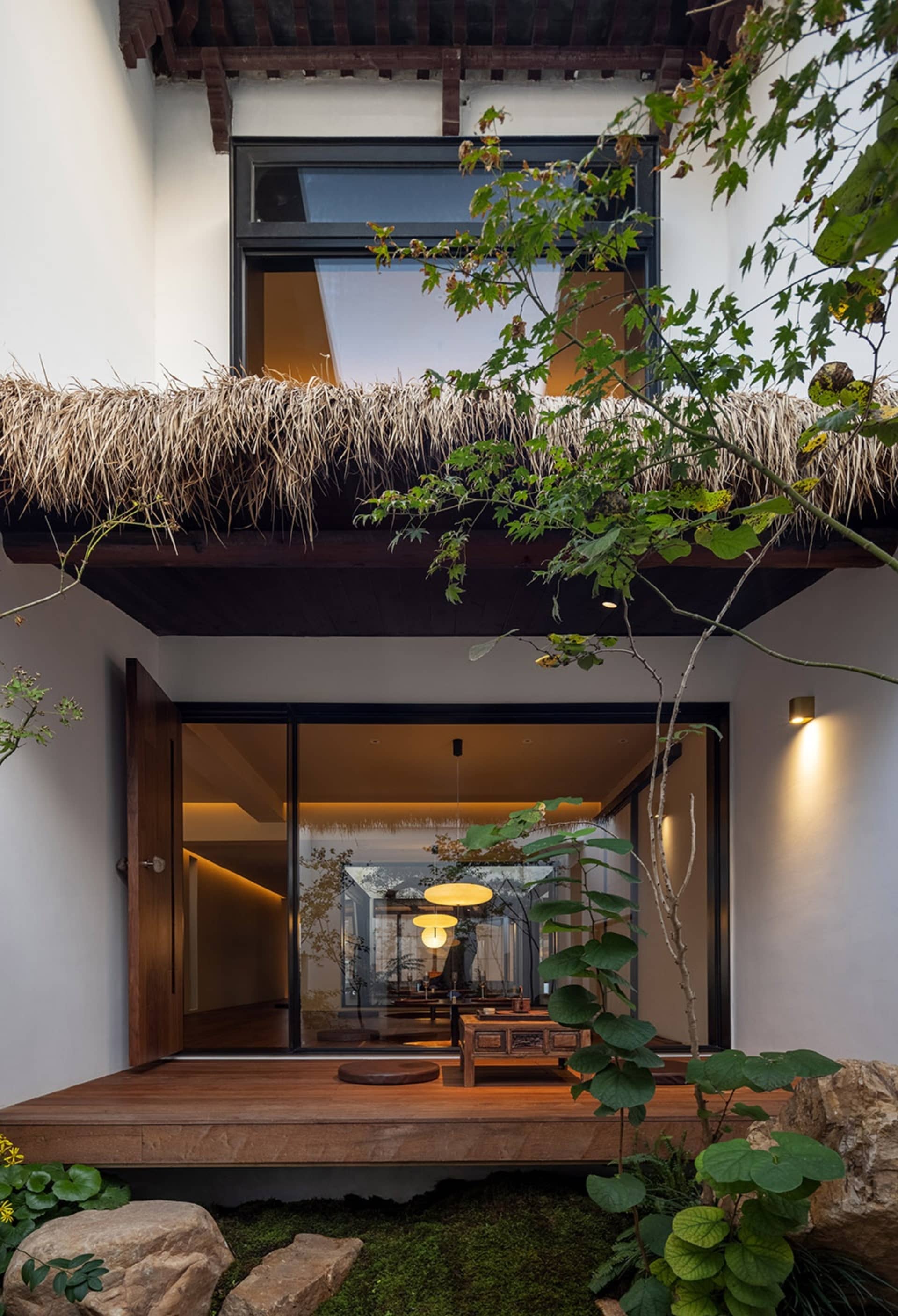 Warm and inviting living area with a wooden floor, straw roof, two chairs, a dining table, and a potted plant