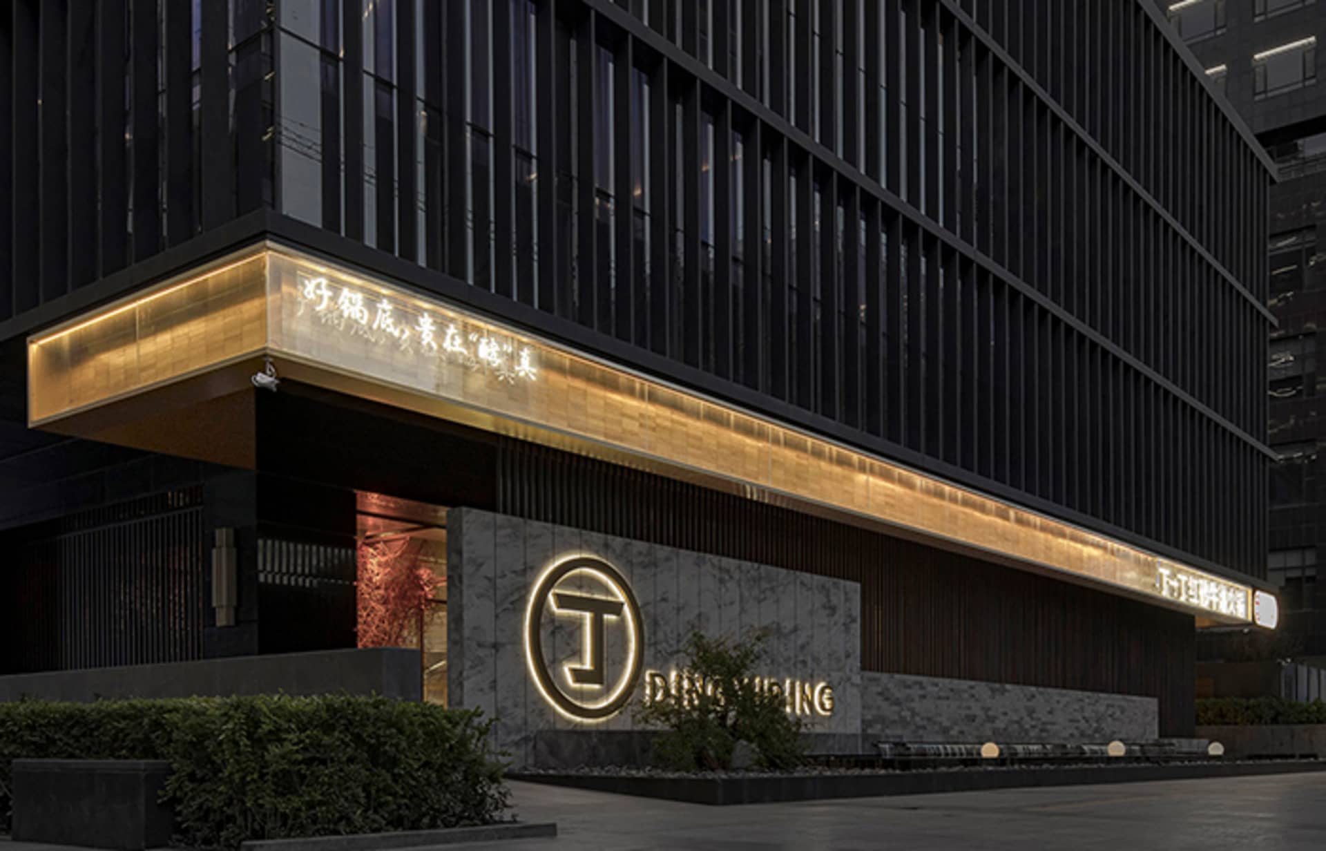 Modern office building with a black facade, lit windows, and a bench in front