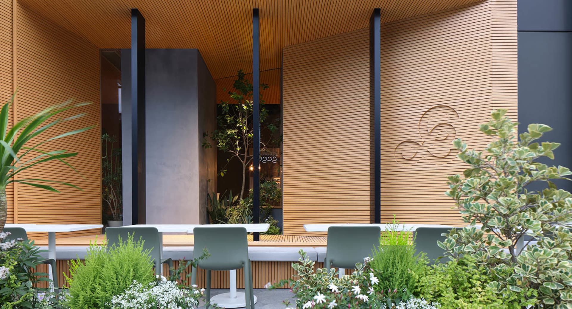 Cozy indoor dining area with two green chairs near a table, surrounded by potted plants and a warm atmosphere