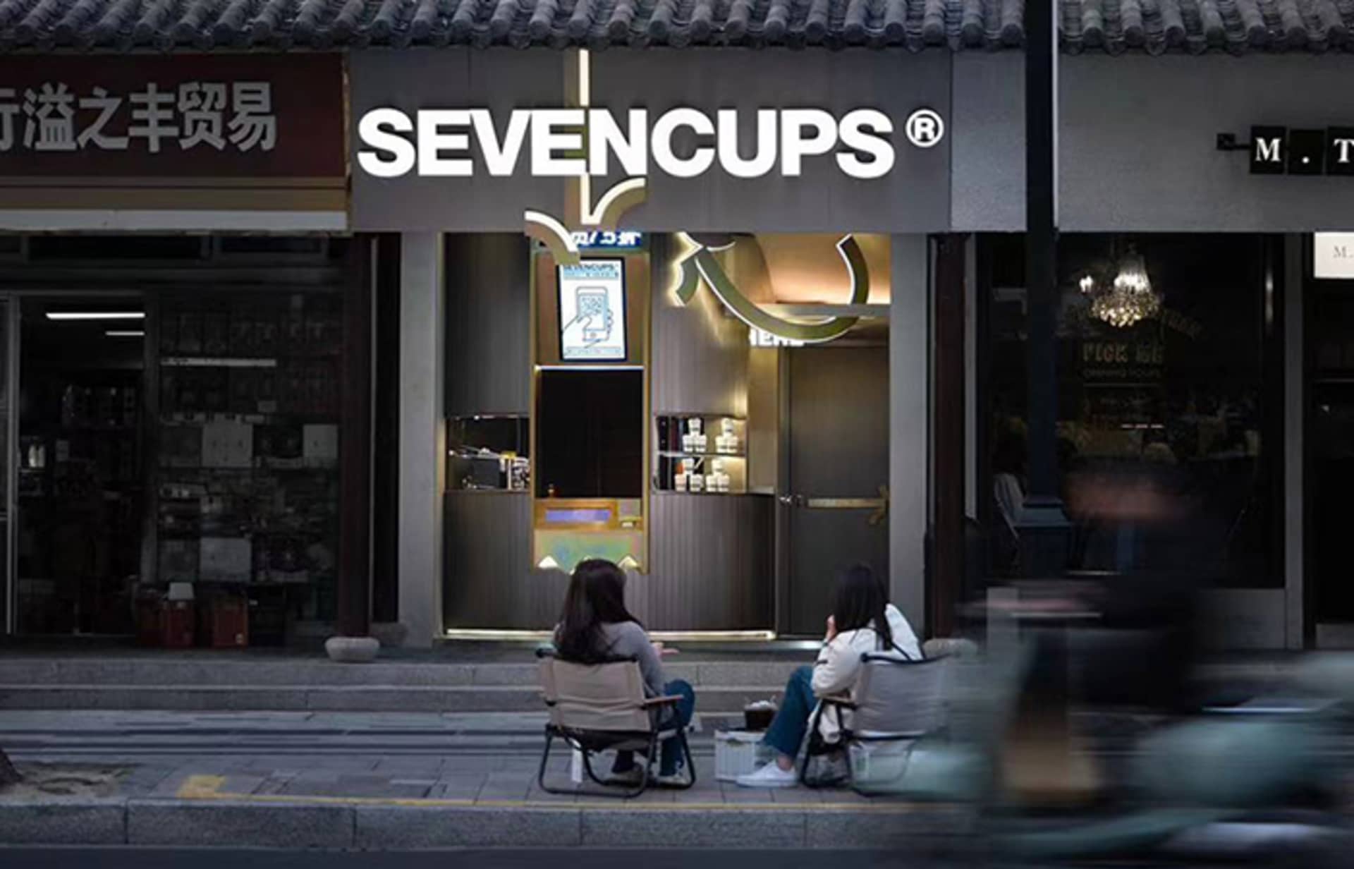 Two women enjoying drinks outside a cozy Asian restaurant with wooden elements