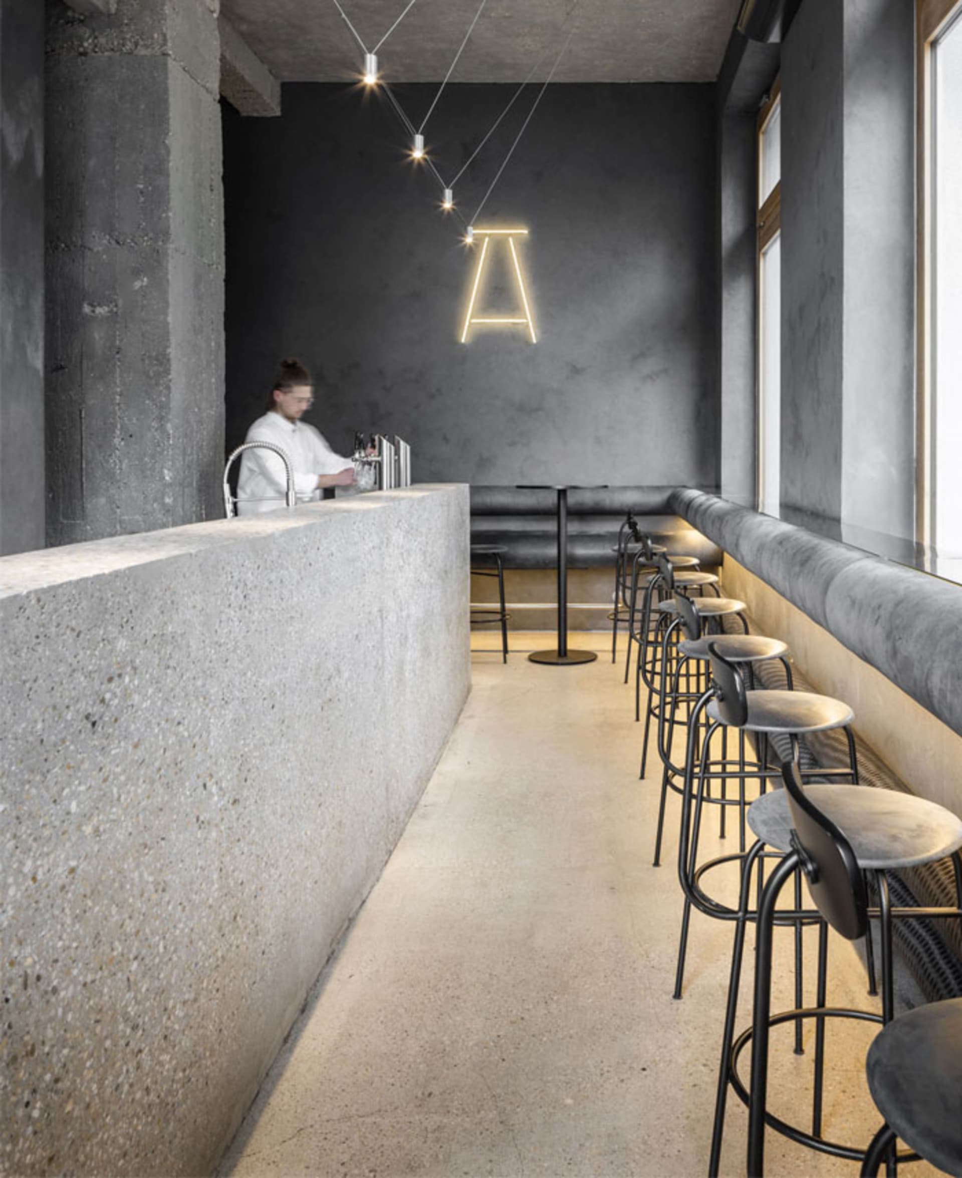 Modern bar area with grey walls, black stools, and a dining table, surrounded by chairs and providing a comfortable seating space