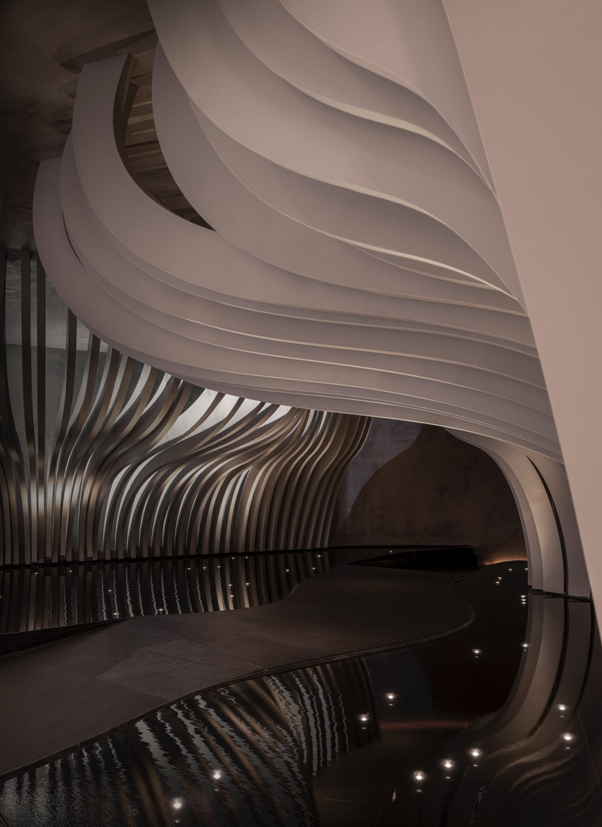 A large, modern interior space with curved walls, reflective surfaces, and a minimalist atmosphere, featuring clean lines and sleek surfaces, with ample open area and dim lighting