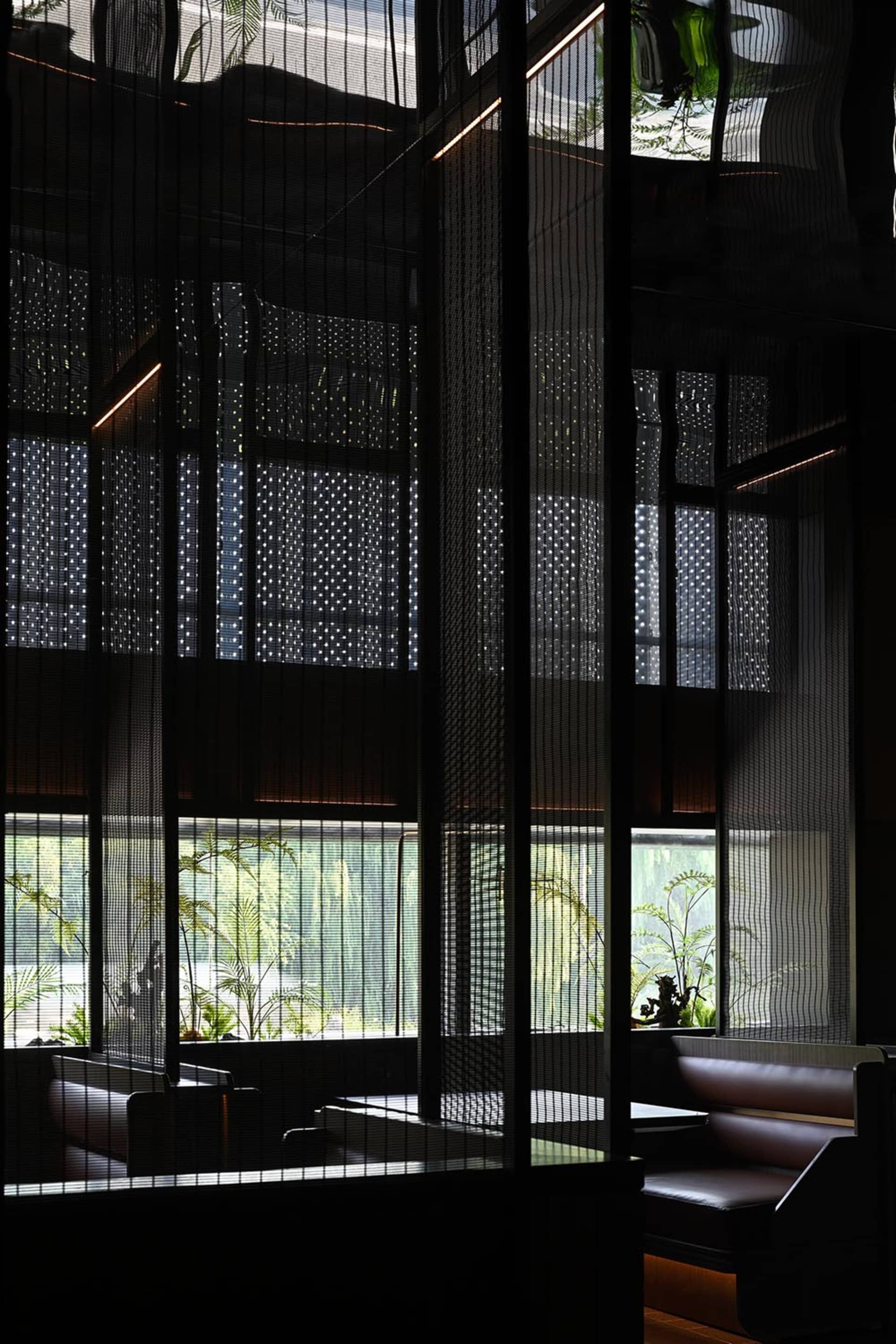 Modern restaurant dining area with black walls, potted plants, and minimalist decor