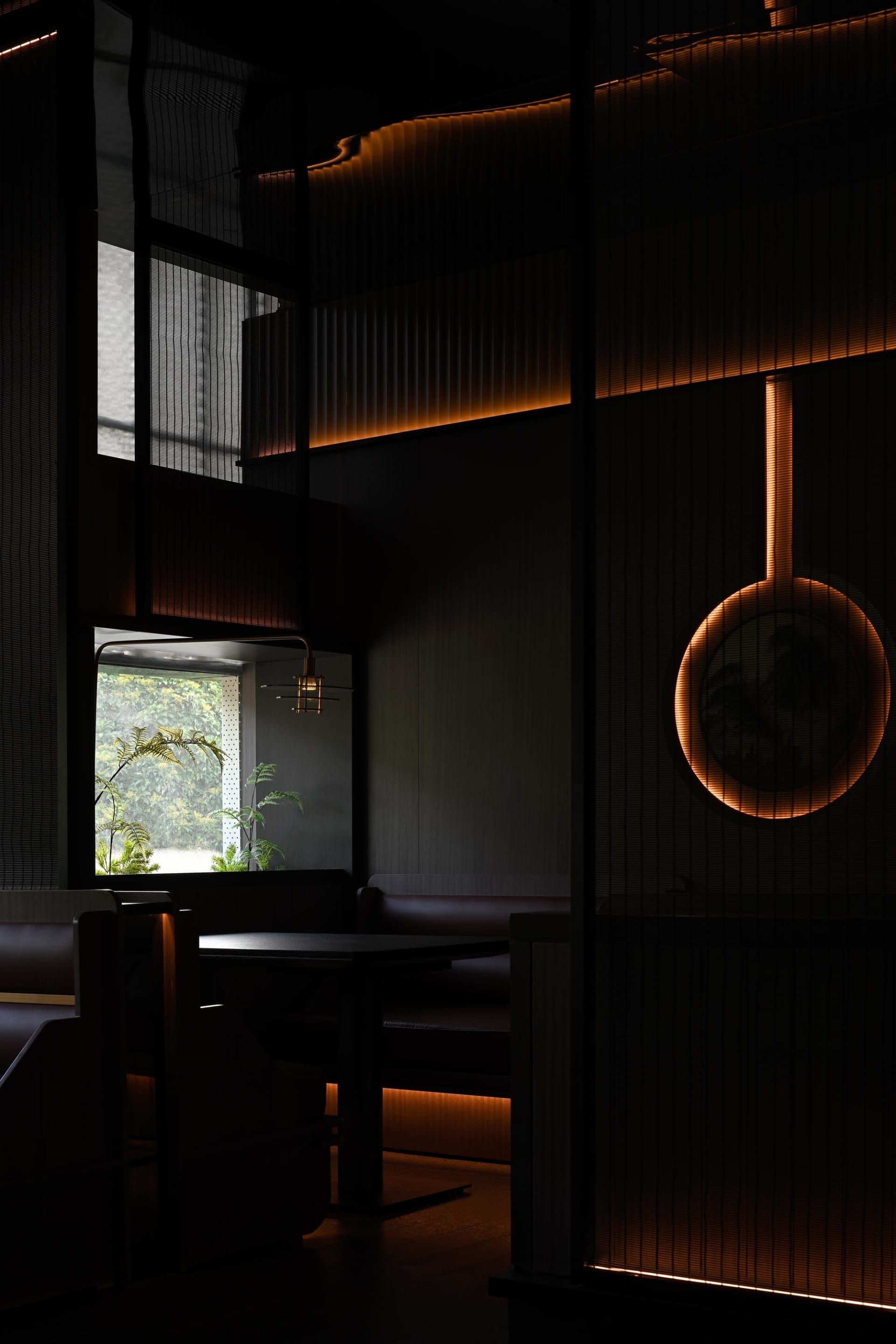 A cozy restaurant dining area with black walls, natural light, and a large table surrounded by chairs