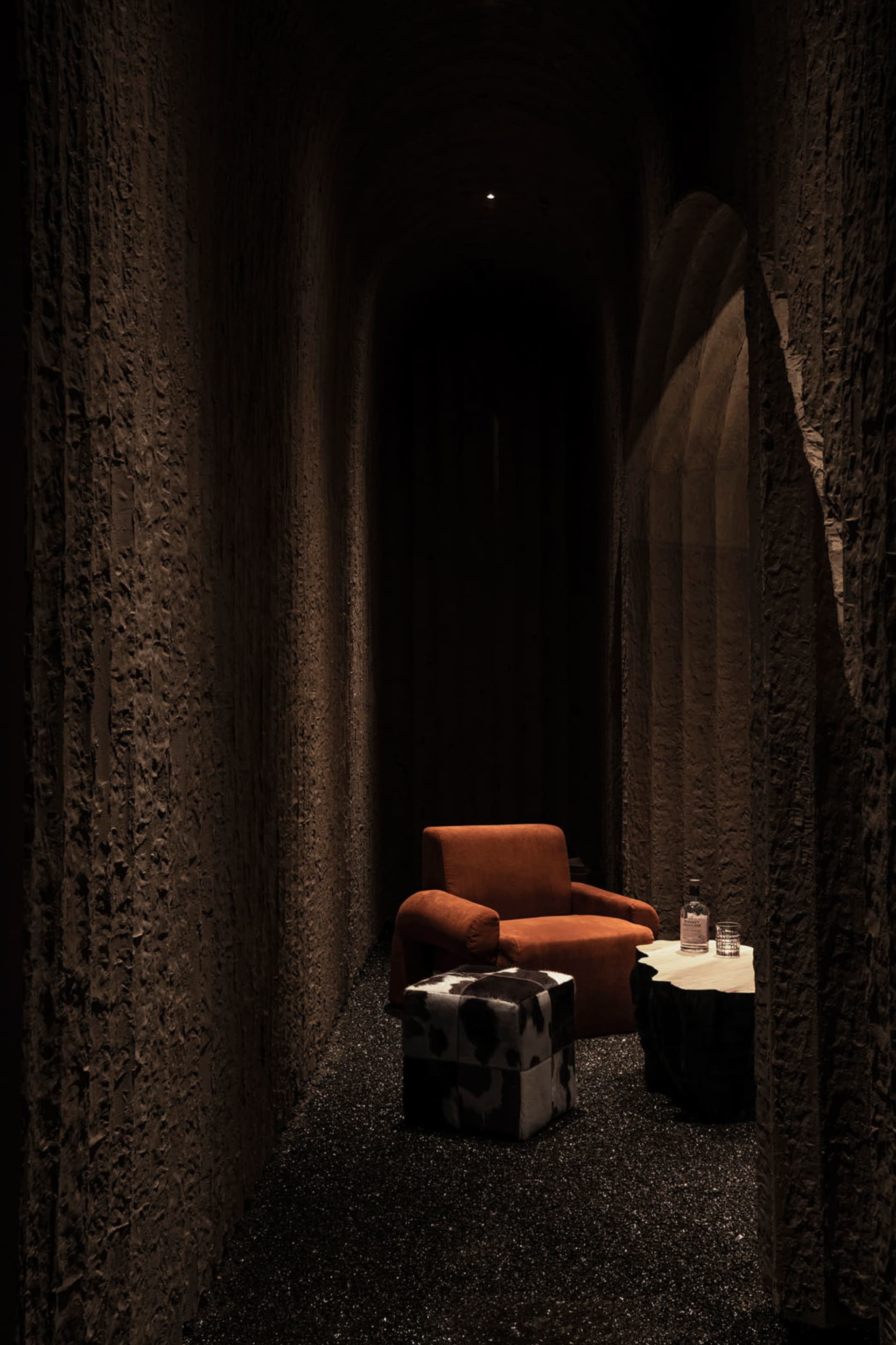 Cozy living space with an orange chair, a table with a bottle, and rock wallpaper on the walls