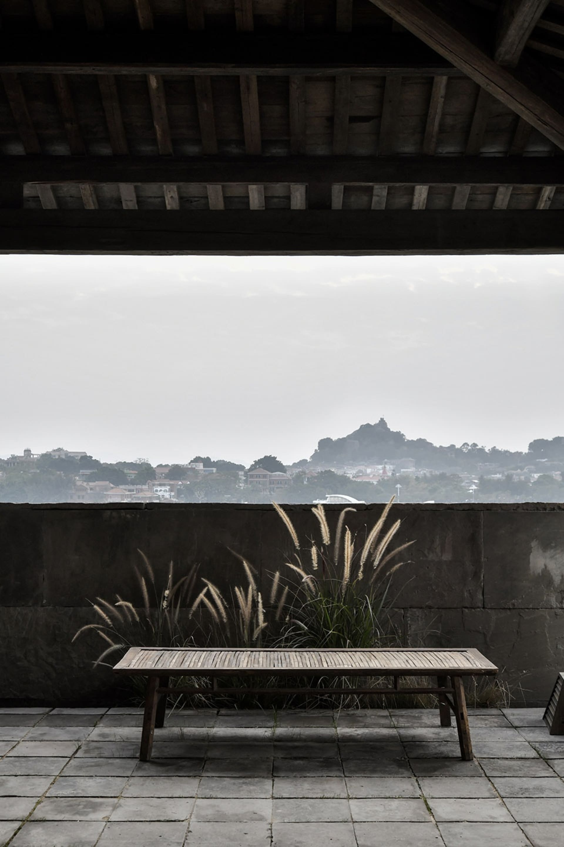 A wooden table and bench sit in front of a window overlooking a mountainous cityscape