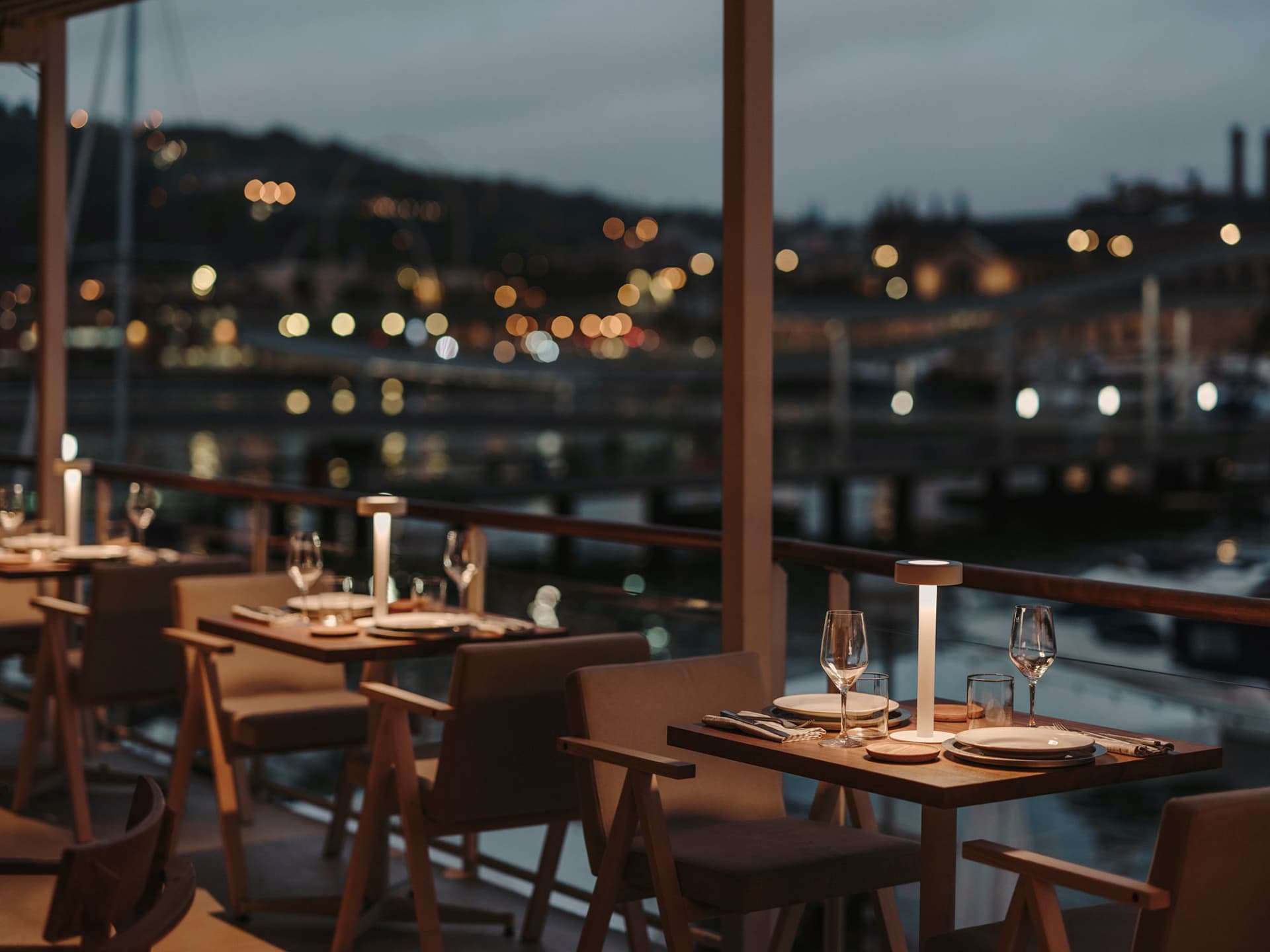 Sophisticated dining space with tables, chairs, wine glasses, and cutlery, featuring a combination of wood and metal elements, warm lighting, and a cozy ambiance