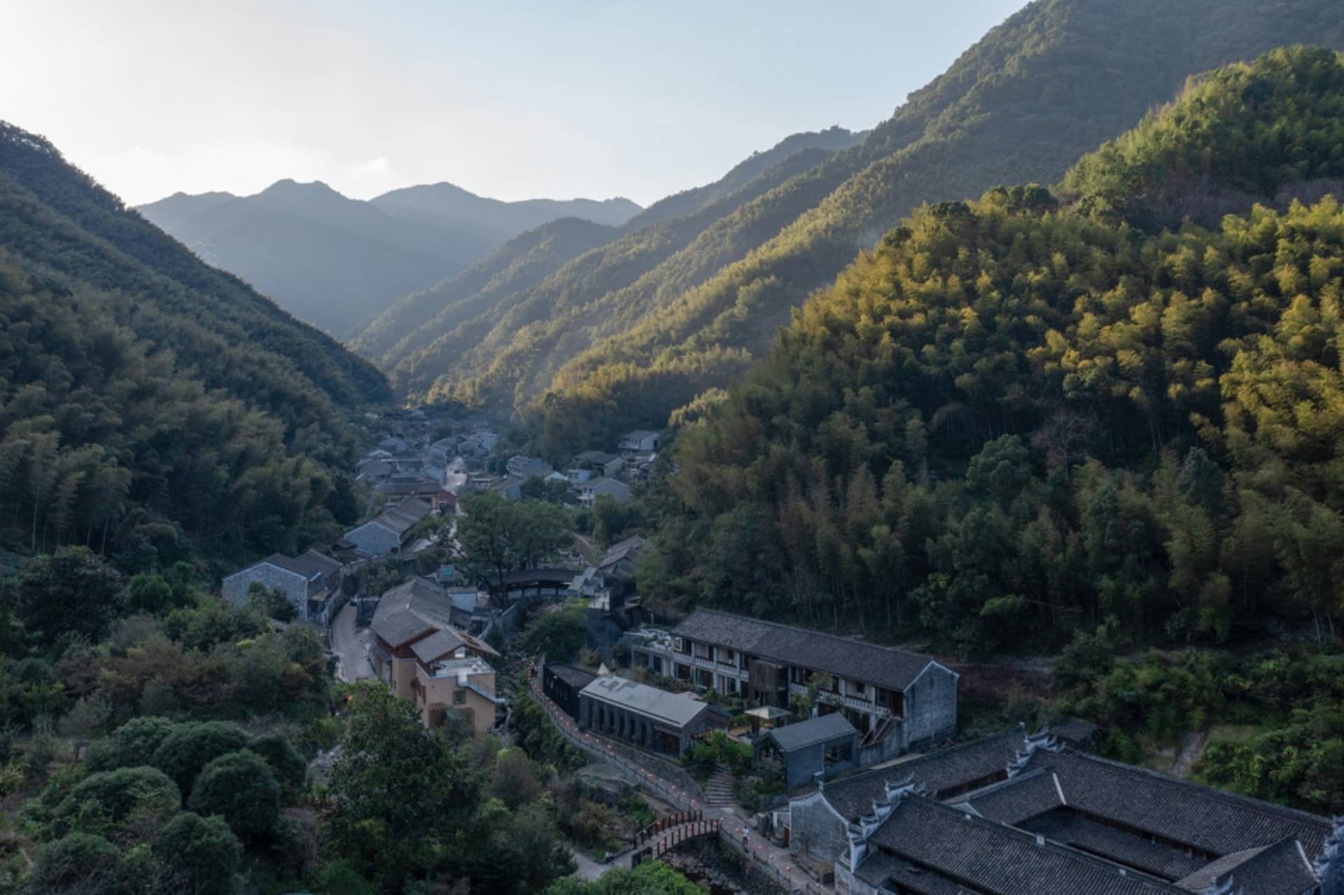 A serene village nestled in a valley surrounded by mountains, featuring traditional buildings and lush greenery