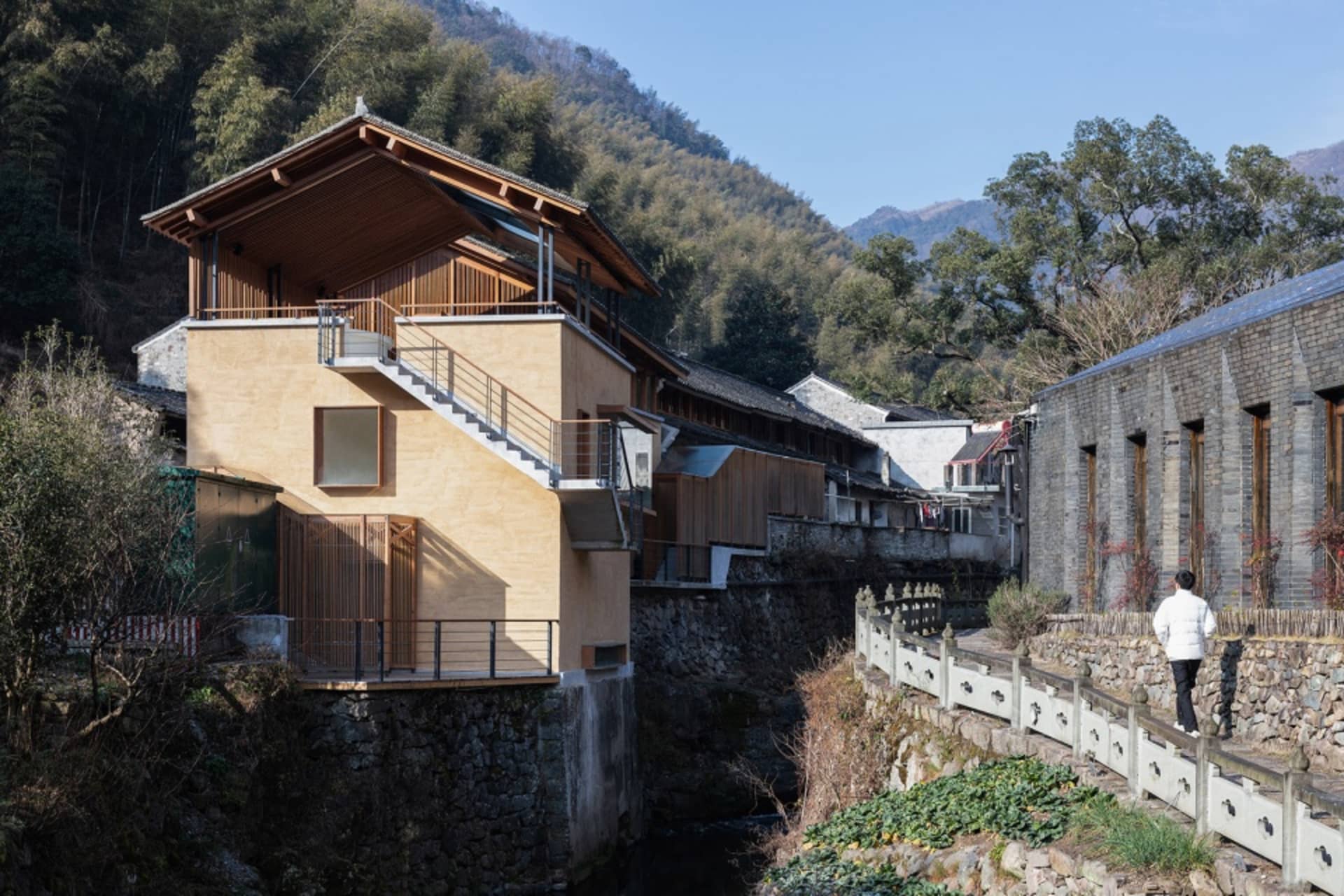 A yellow house with a balcony and staircase in a mountainous area, featuring two benches and a cozy atmosphere