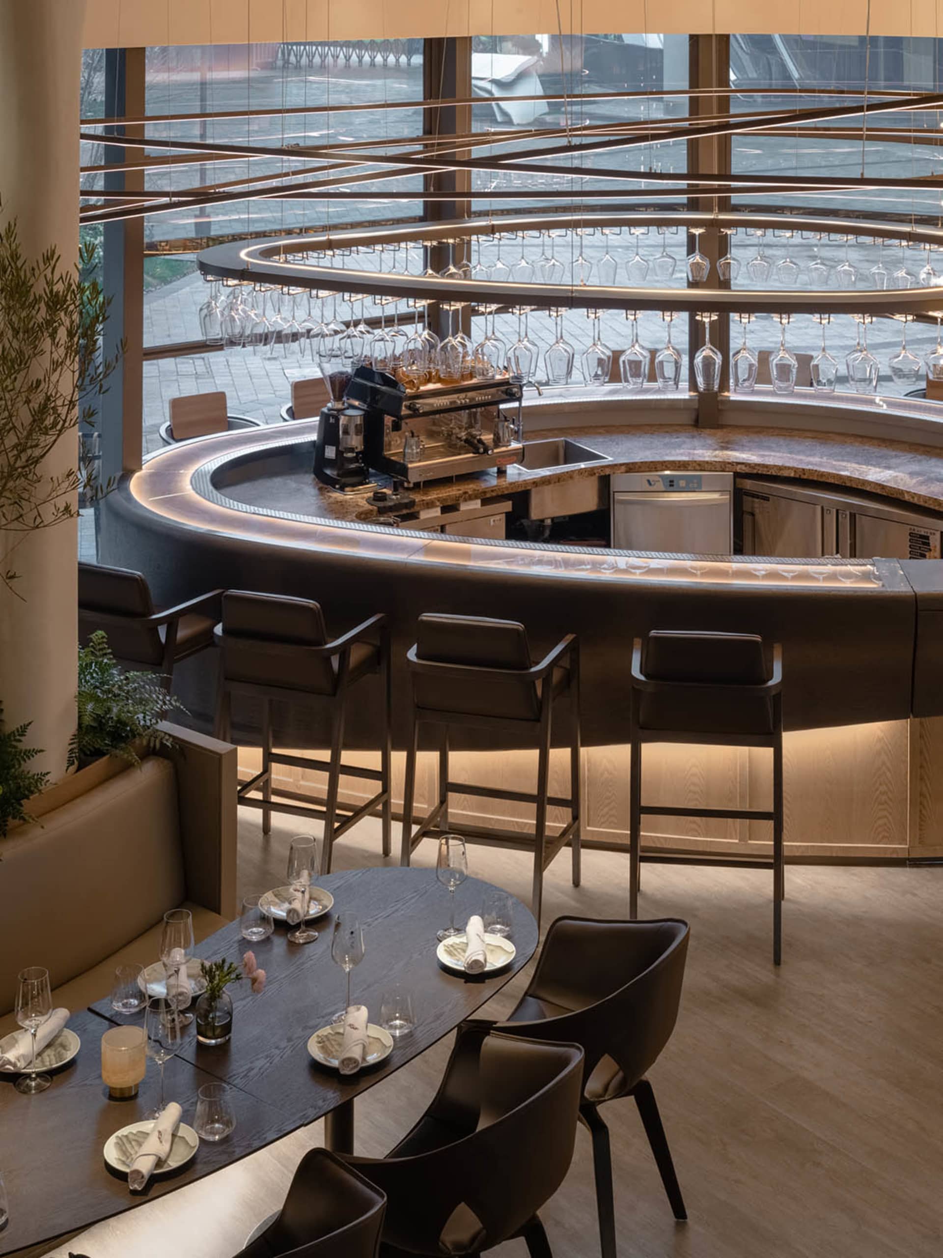 A modern bar area with a circular counter, wine glasses, and seating for patrons