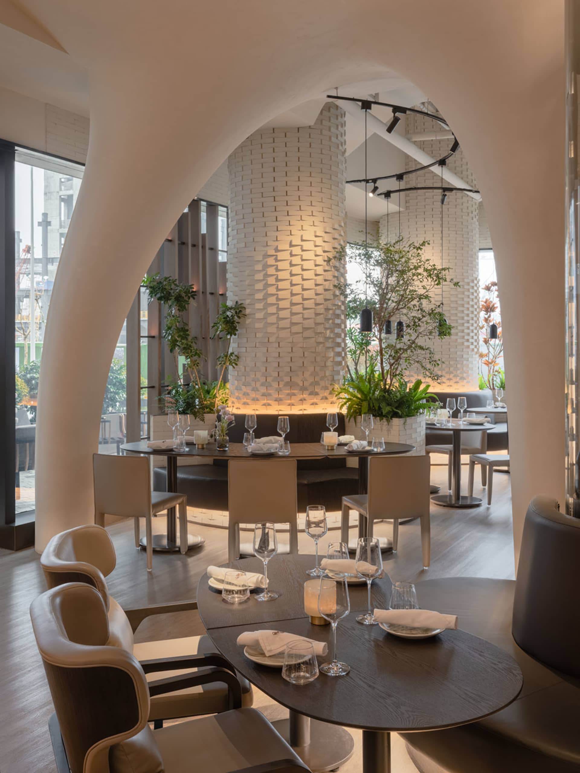 Modern restaurant interior with white tile walls, potted plants, and a large dining area with tables and chairs