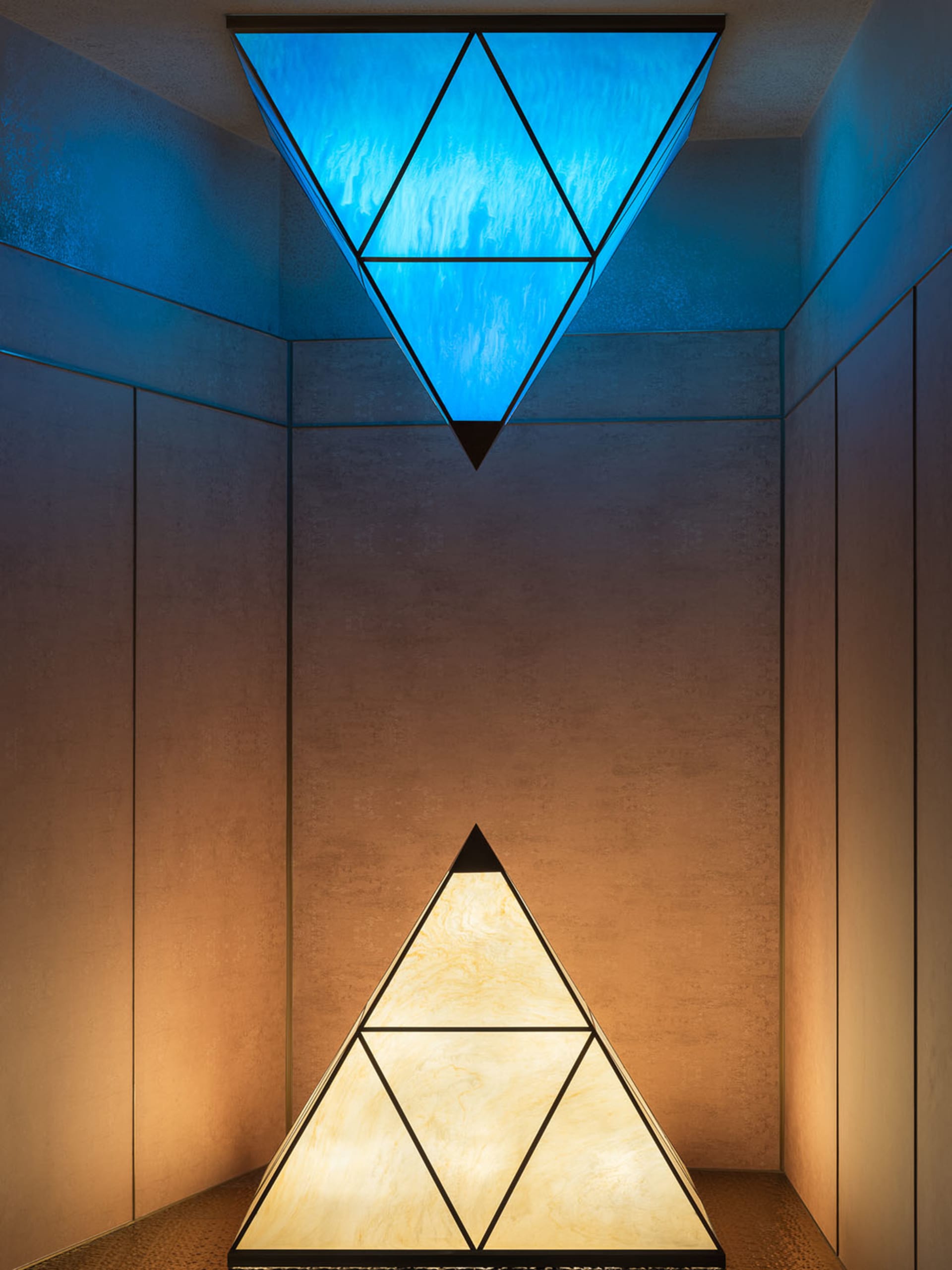 A modern room with two glass triangular lamps or decorative elements, illuminated by artificial light, creating a warm atmosphere
