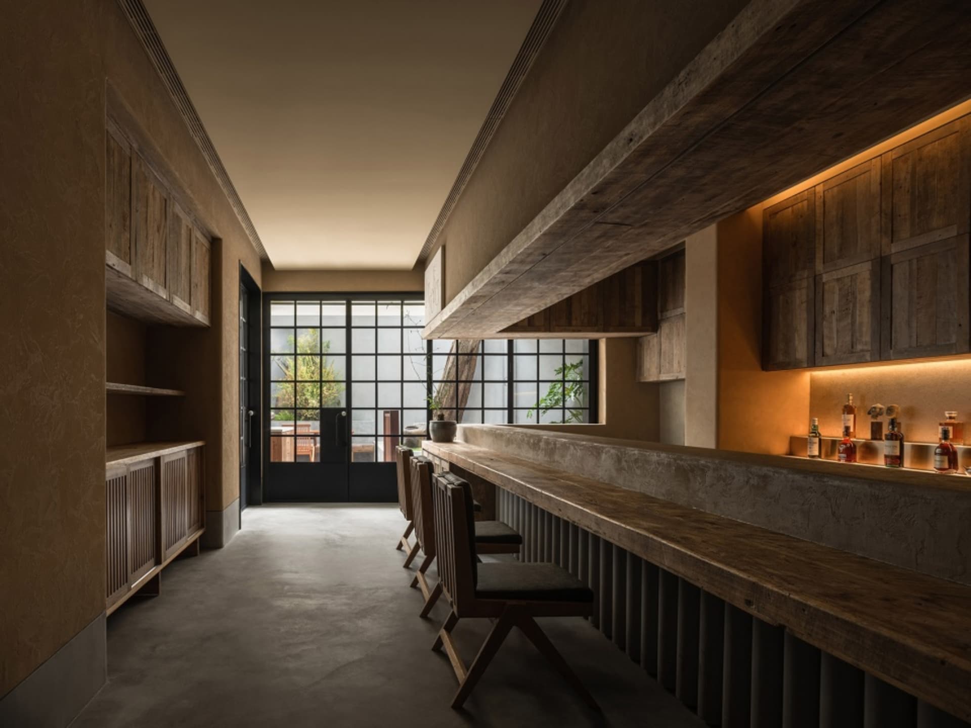 Empty bar area with a long wooden counter and three chairs, giving a sense of calmness