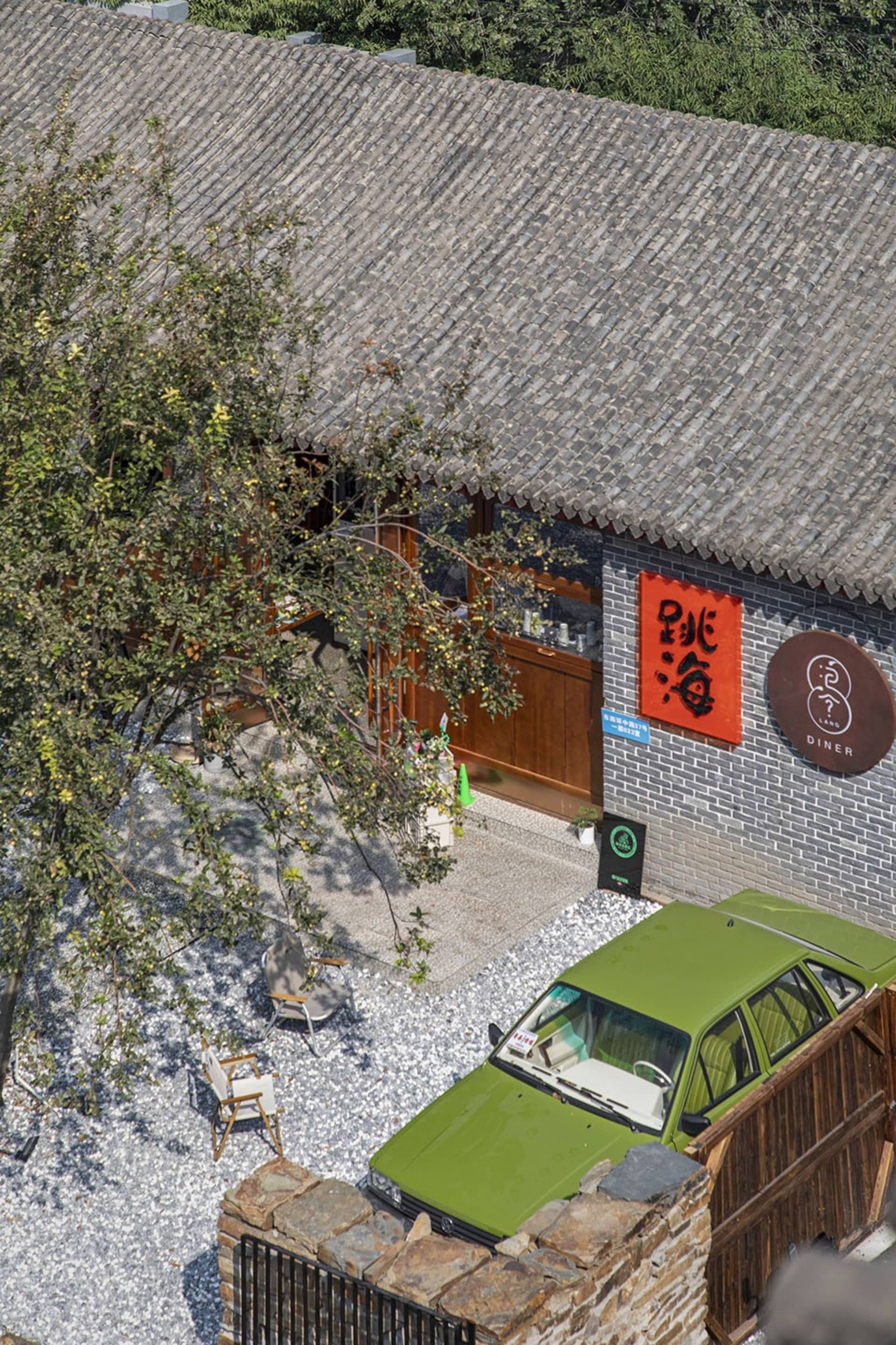 A brick restaurant with a red sign and a green car parked outside, set against a natural background