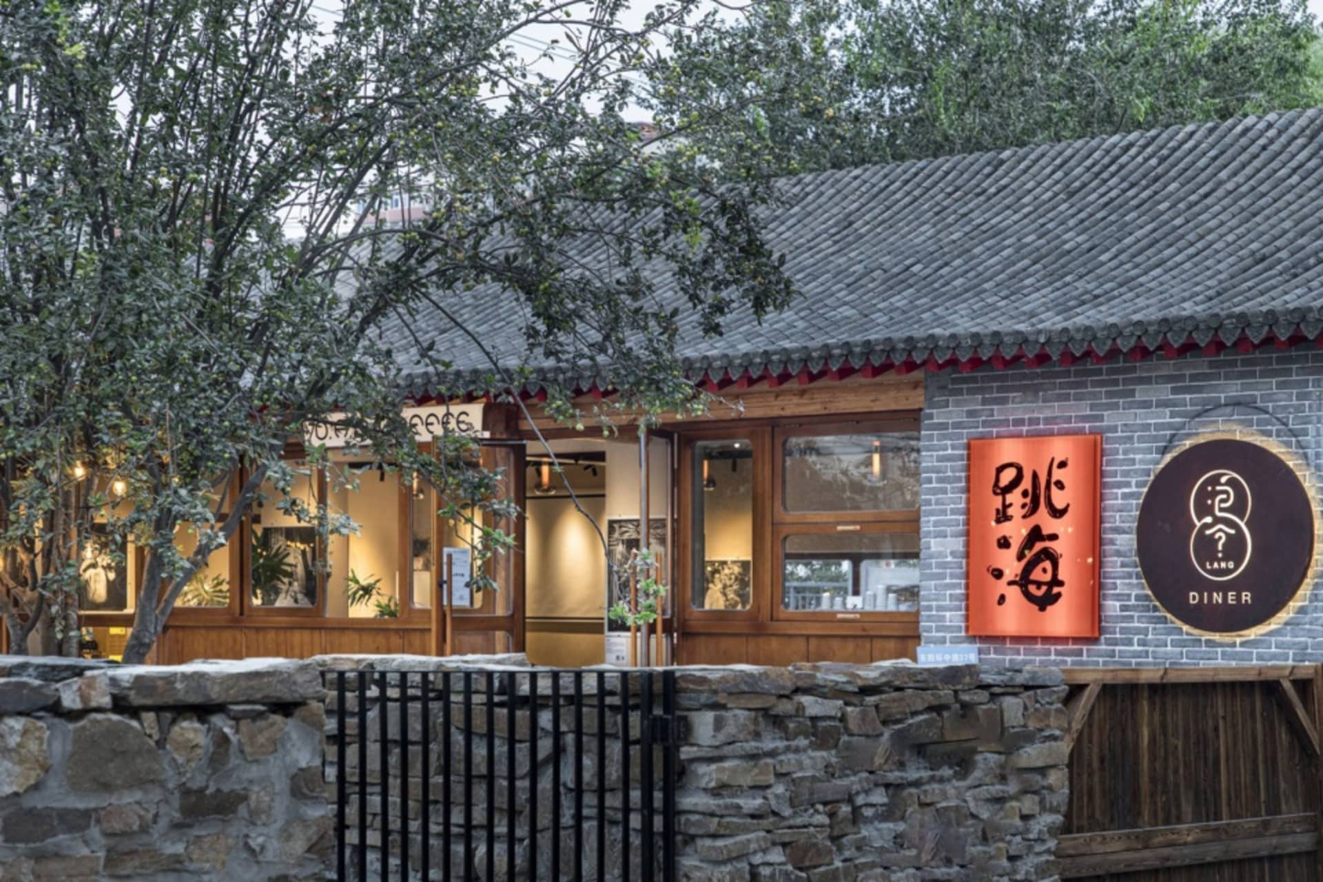 A well-lit Asian restaurant with a stone exterior, red roof, large window, and potted plants inside