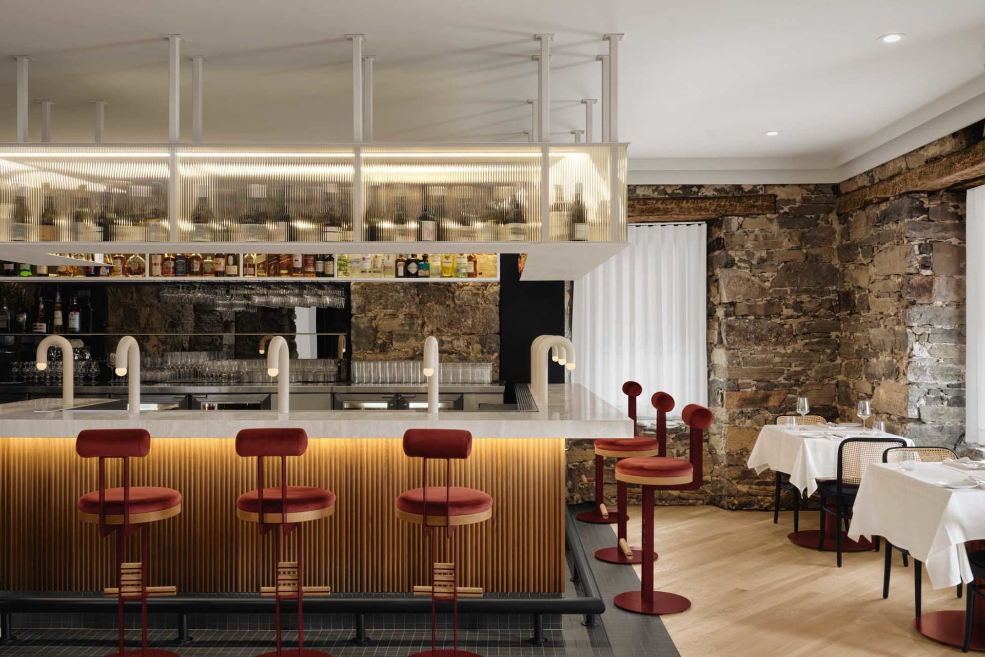 A cozy bar area with a long wooden counter, red stools, bottles, and wine glasses, creating an inviting atmosphere for patrons