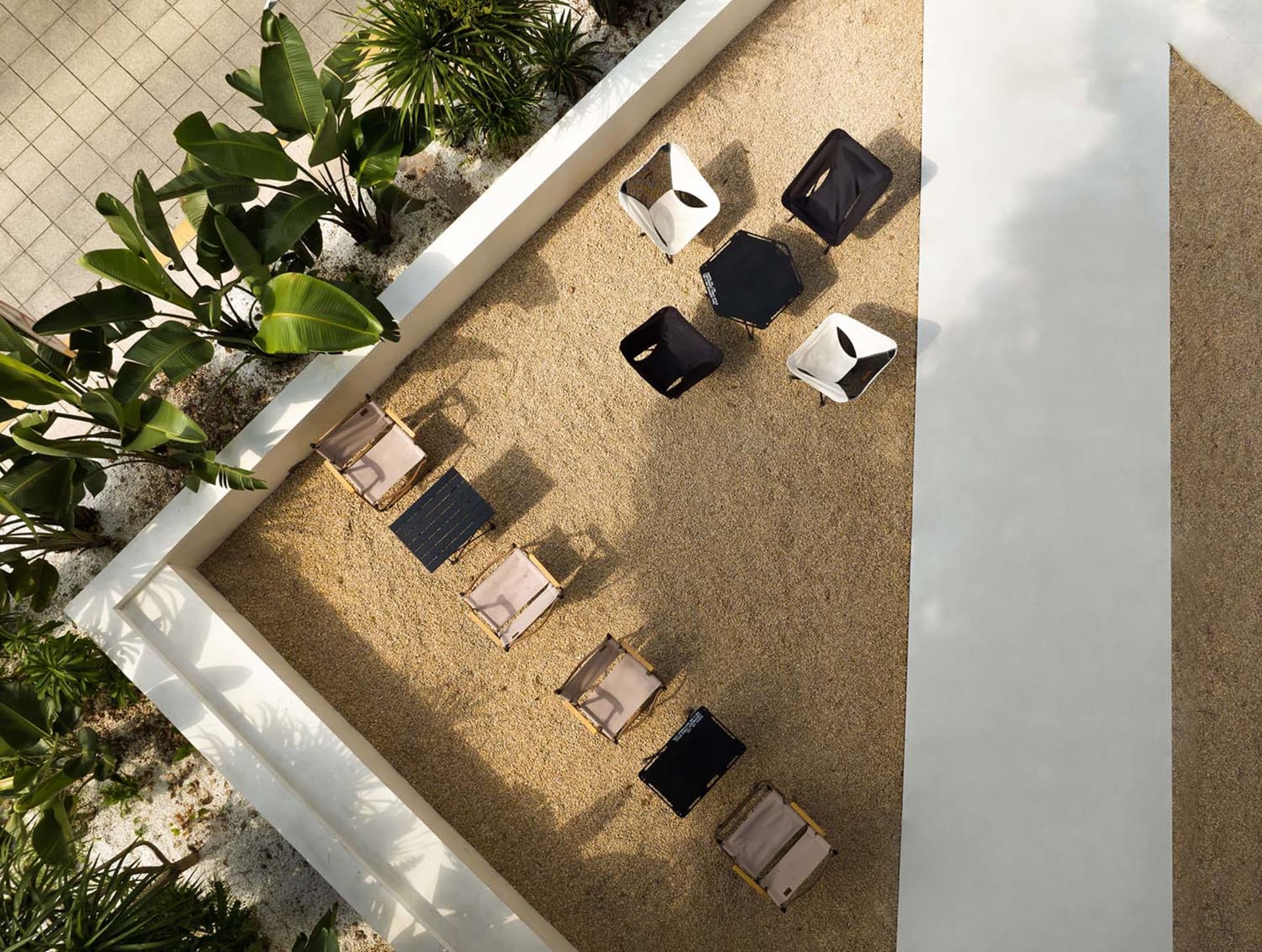 A casual outdoor seating area with black lounge chairs and potted plants on a sandy ground, conveying a relaxed atmosphere