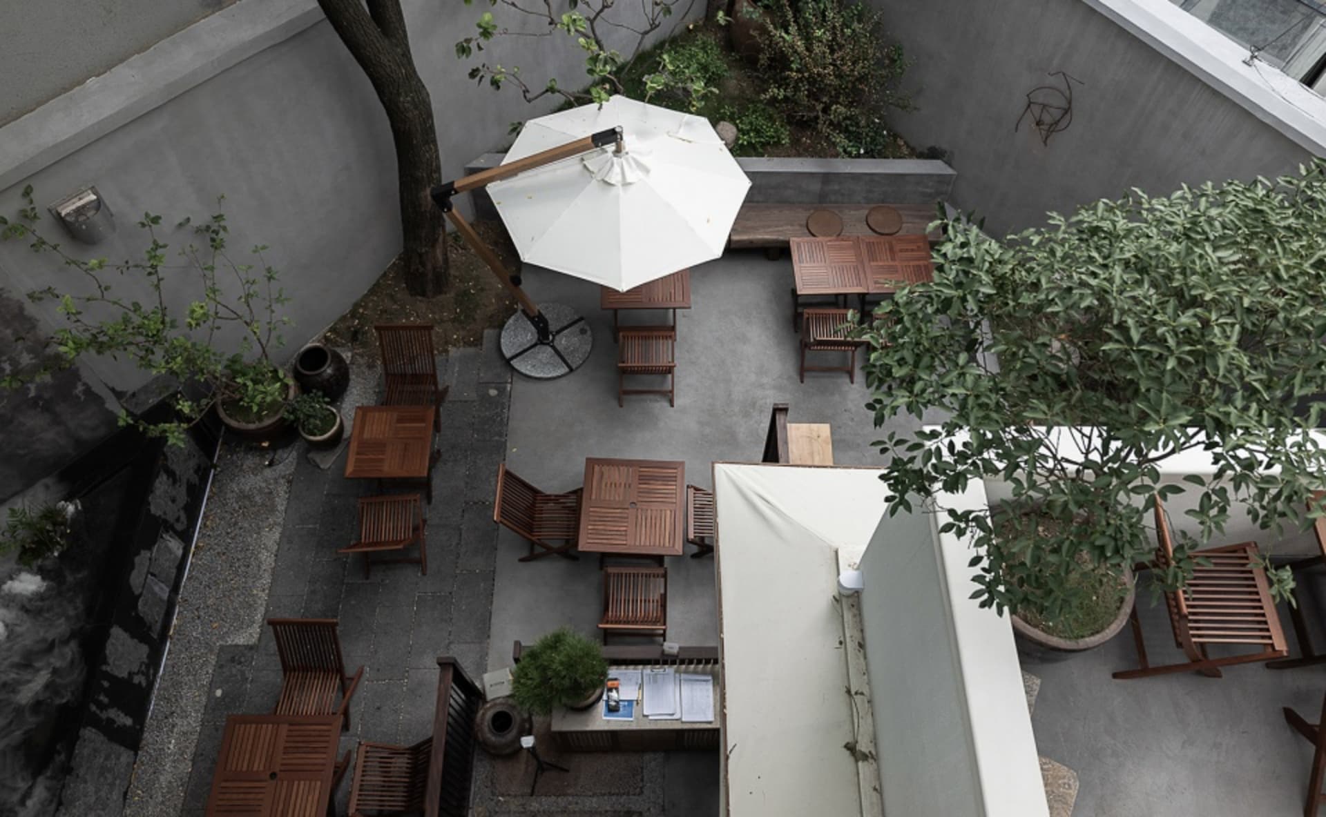 Outdoor dining area with multiple tables and chairs under a large umbrella, surrounded by a relaxed and inviting atmosphere