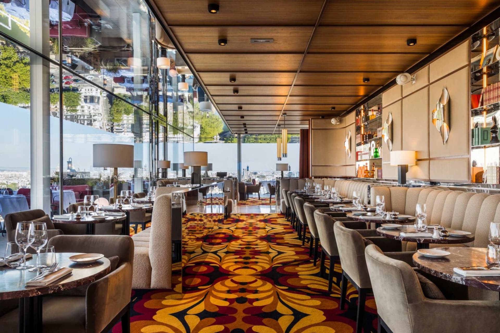 Sophisticated restaurant interior with dining tables, chairs, and wine glasses, featuring carpet flooring and wine bottles on the walls