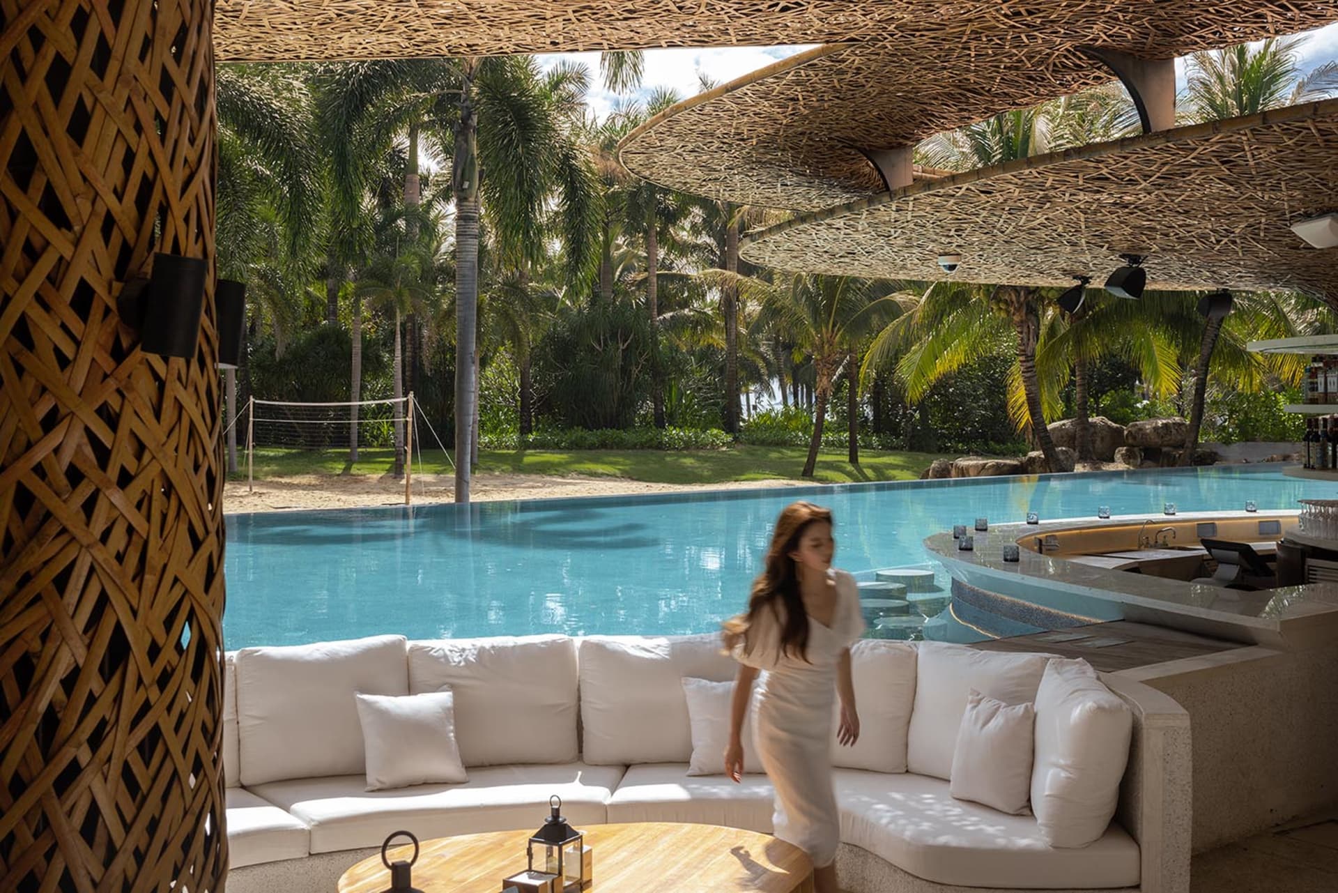 A well-furnished living area with a large couch, dining table, and pool in the background, creating a cozy and inviting atmosphere