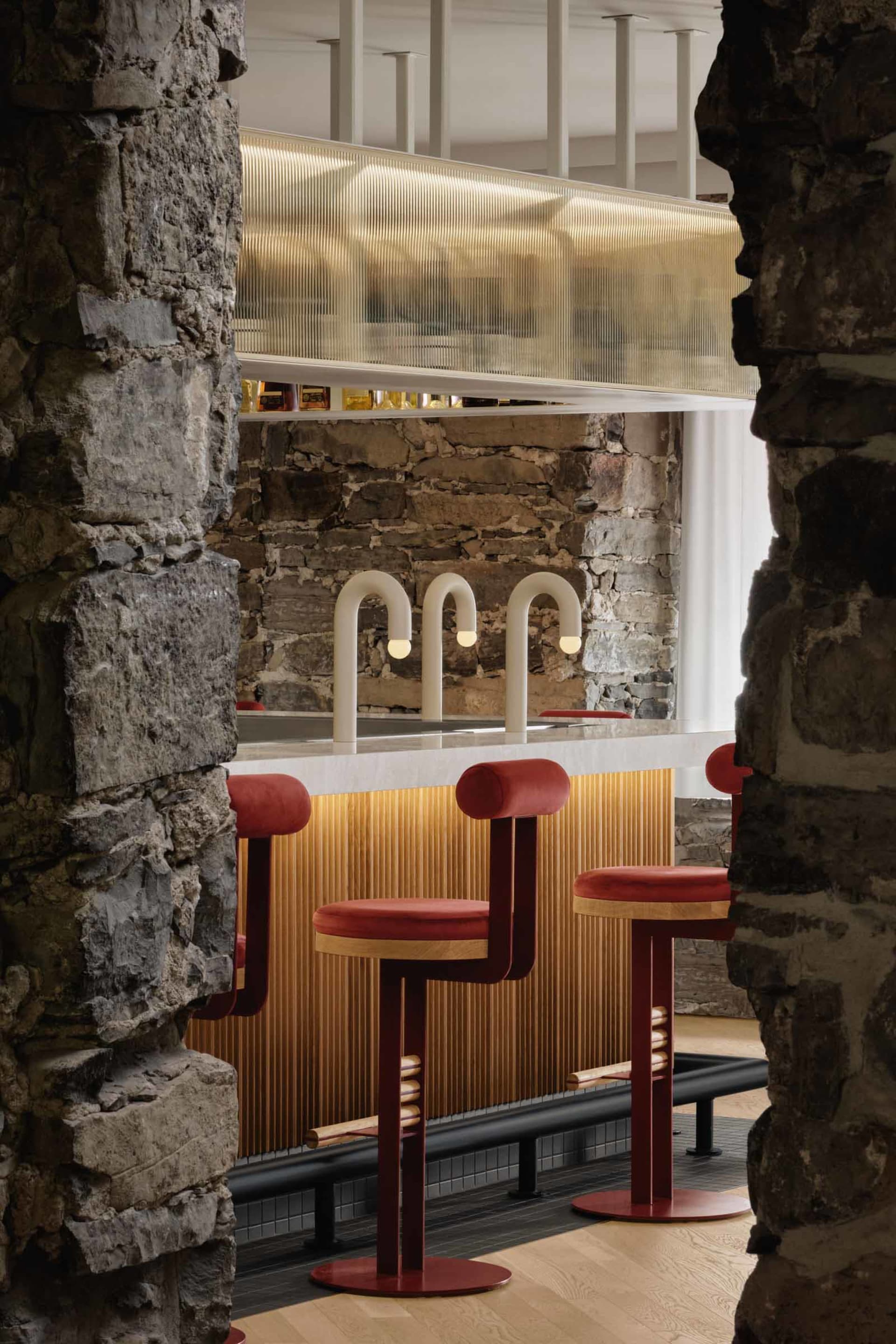 A cozy bar area with a counter and two red stools, featuring three sinks and a warm atmosphere