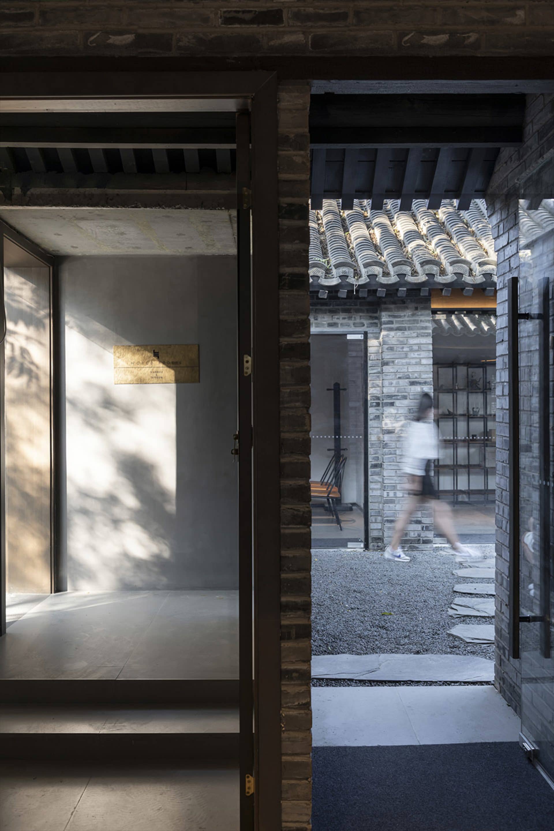 A traditional Asian building with open doors, a brick wall, and a tile roof, featuring a calm and serene atmosphere