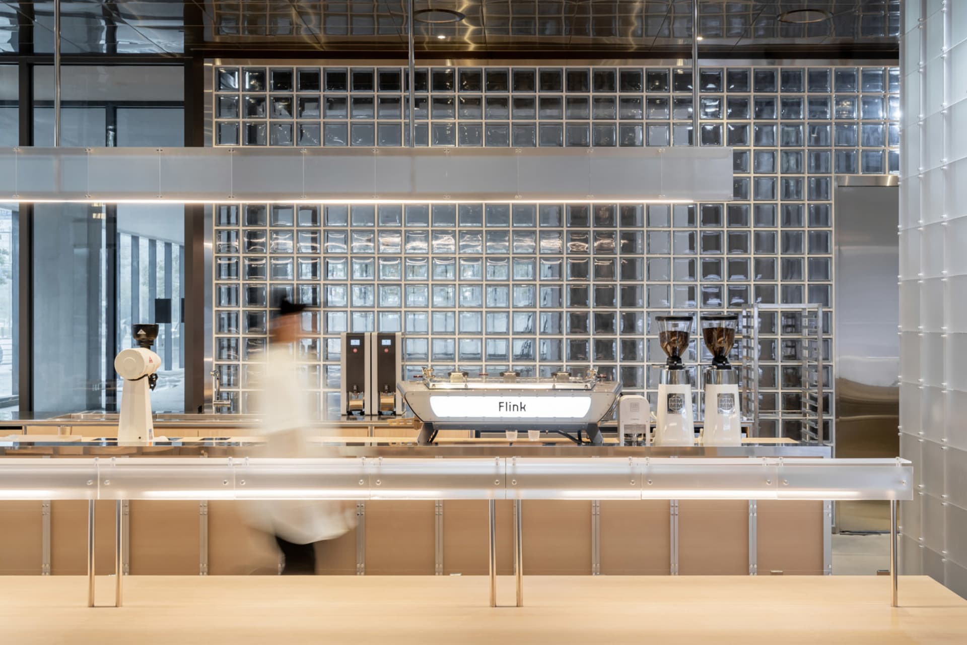 A modern coffee shop with a counter featuring various coffee machines, wood, and metal elements, and a metallic finish on the walls