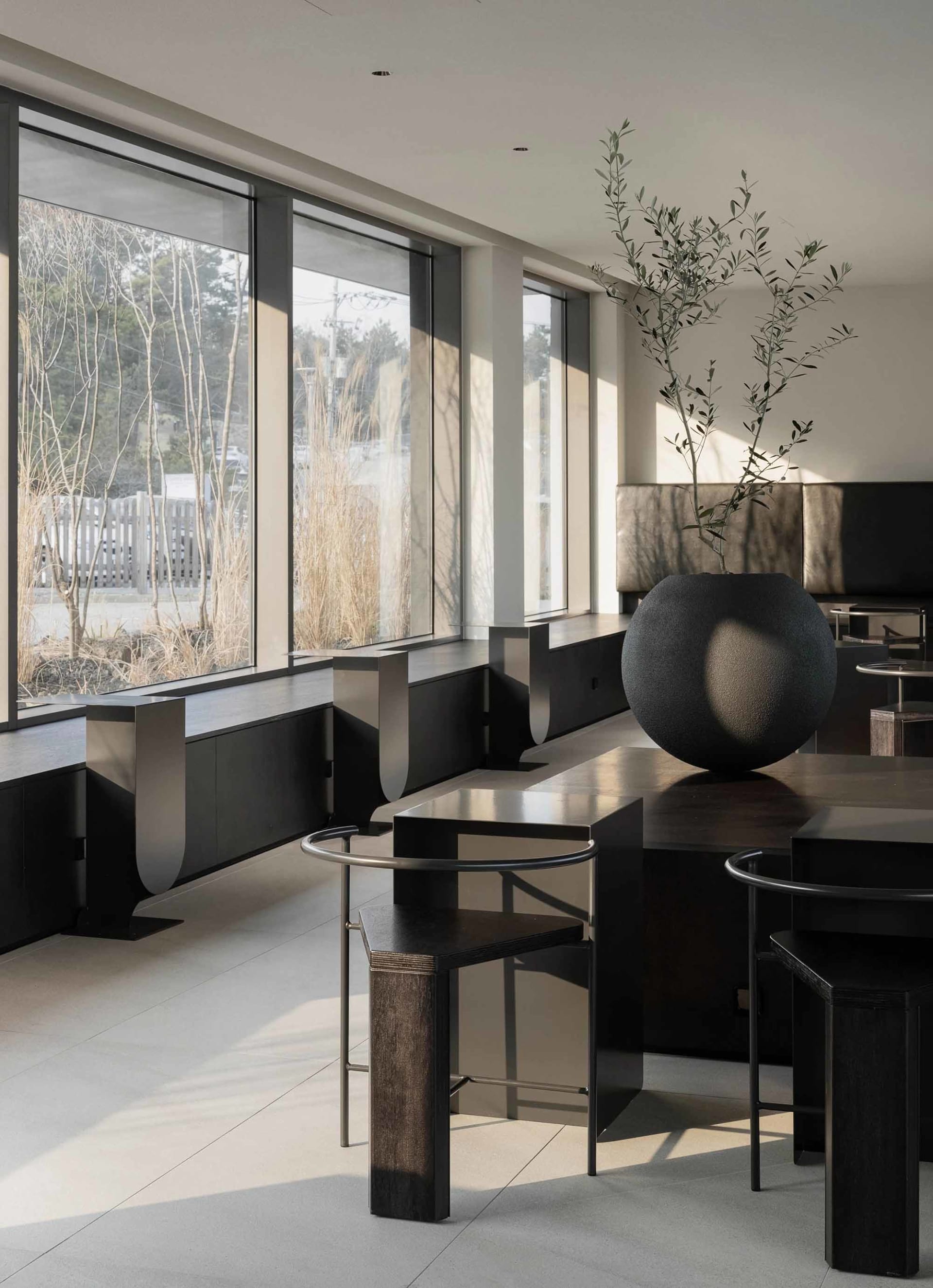A modern restaurant with tables, chairs, and vases, lit by natural light from a large window