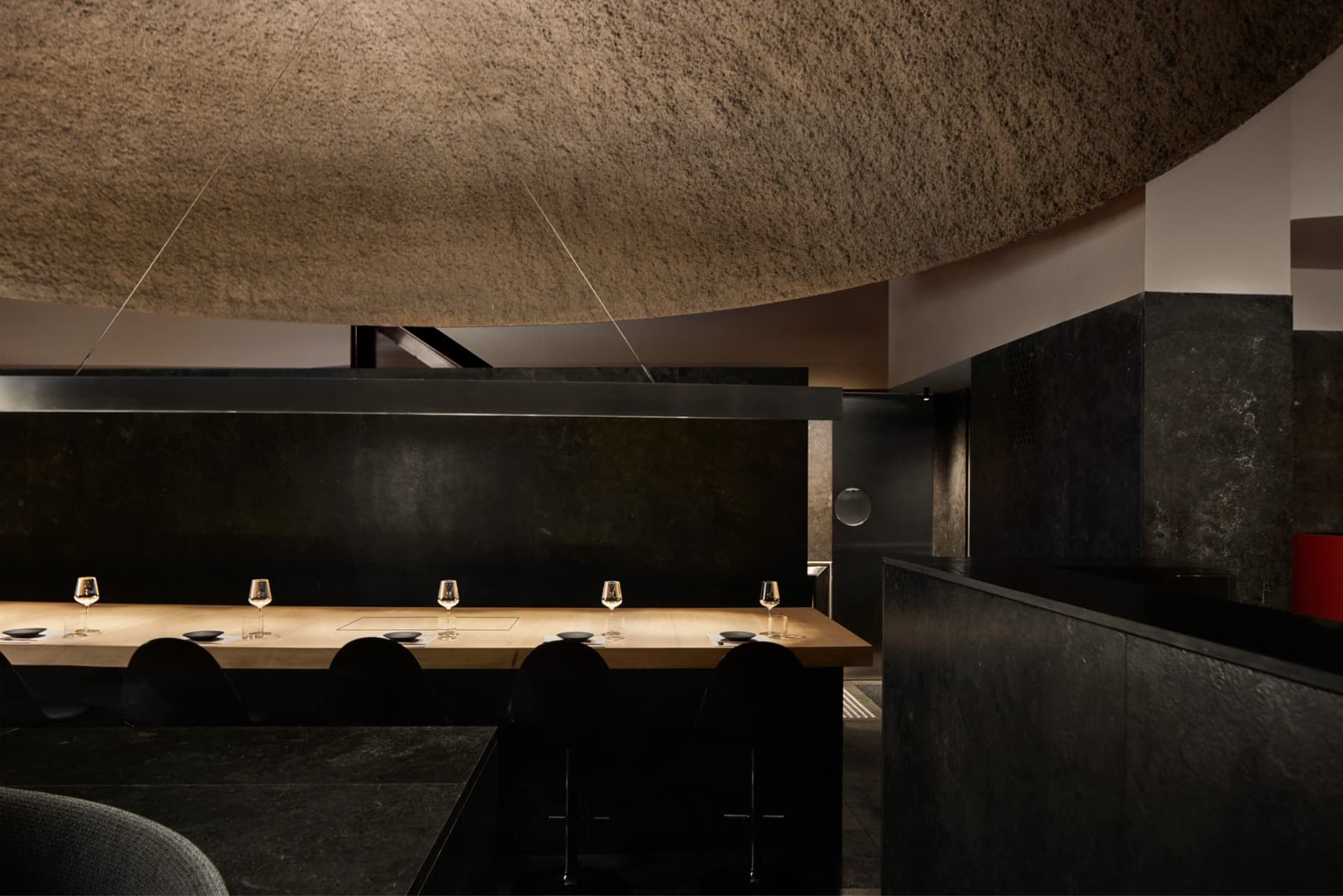 A dimly lit restaurant dining area with a table and chairs, wine glasses, and a moody atmosphere