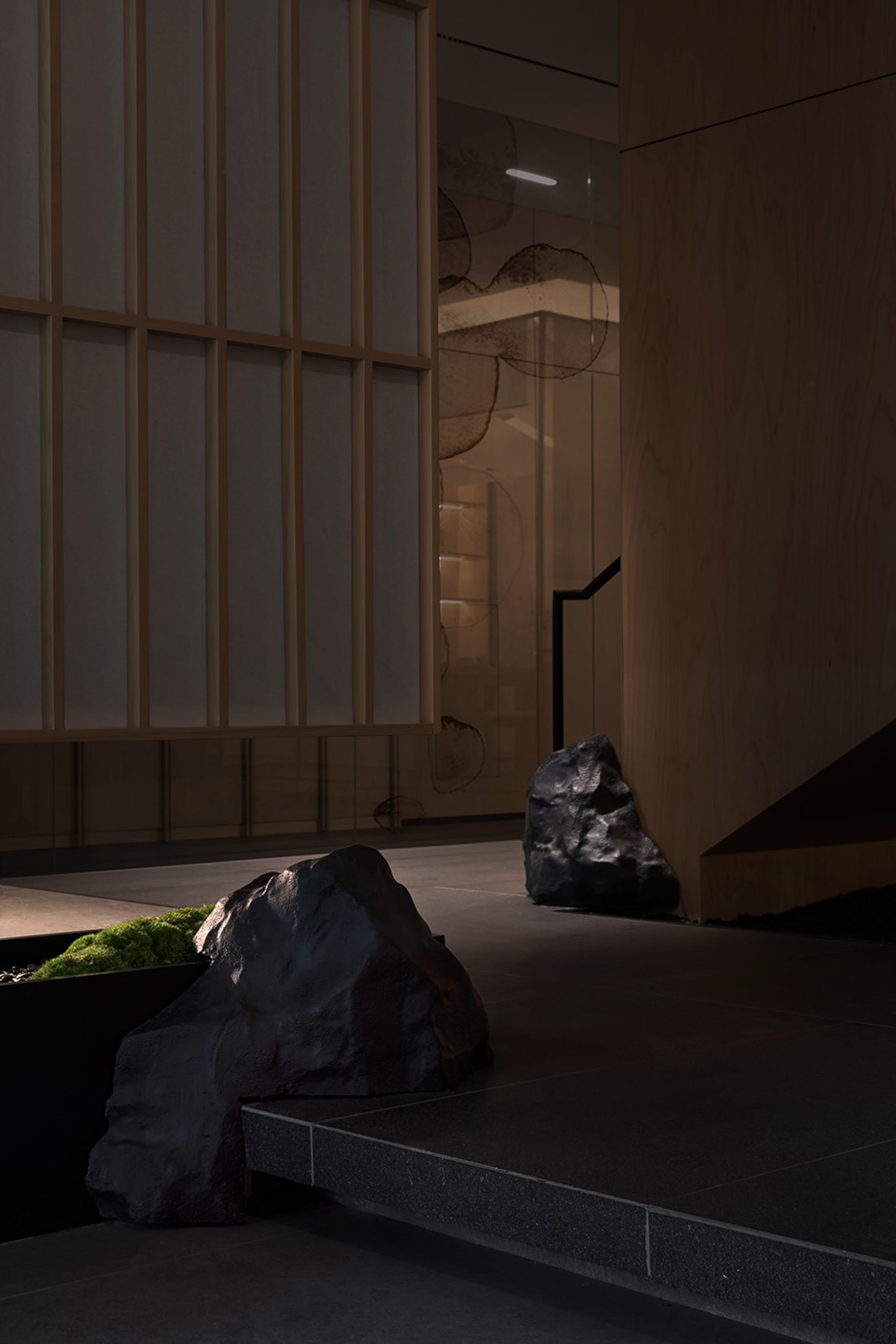 A living room and kitchen area with a black rock wall, wooden staircase, and a dining table with a chair, surrounded by three large rocks