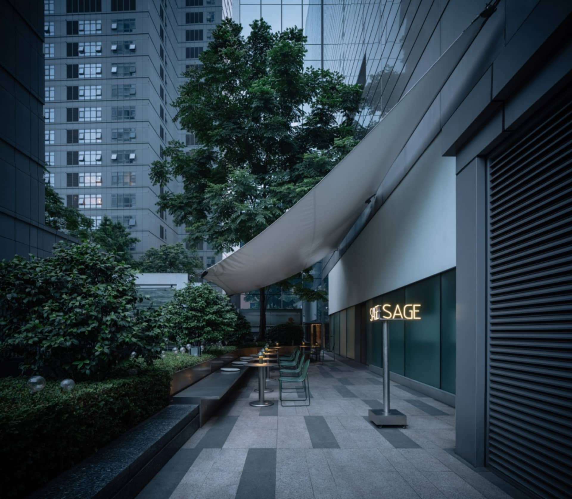 A calm and inviting urban street scene at night with a large building featuring a white awning and outdoor seating area