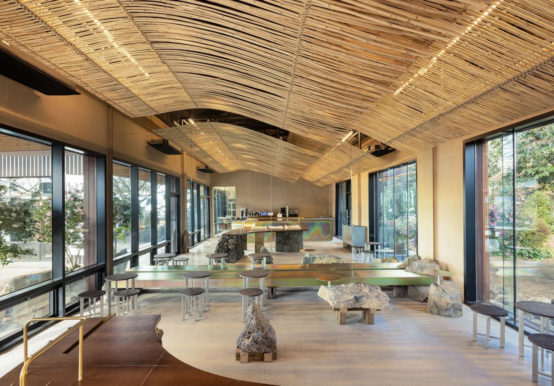 Open restaurant interior with multiple dining tables, chairs, and a bar, featuring wood flooring and a warm atmosphere