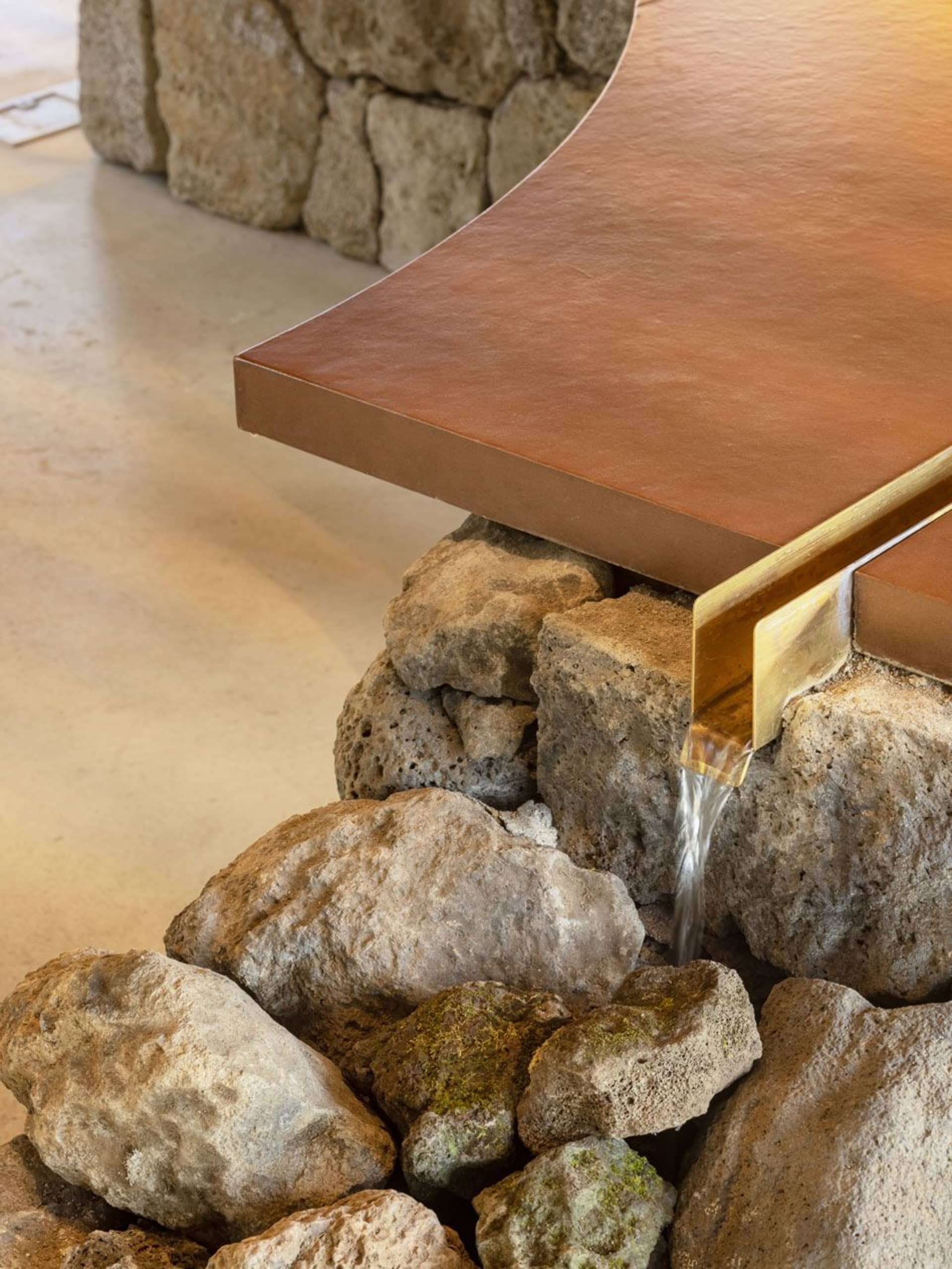 A stone table with a gold trimmed edge and a water feature, surrounded by rocks in a bright and inviting outdoor space