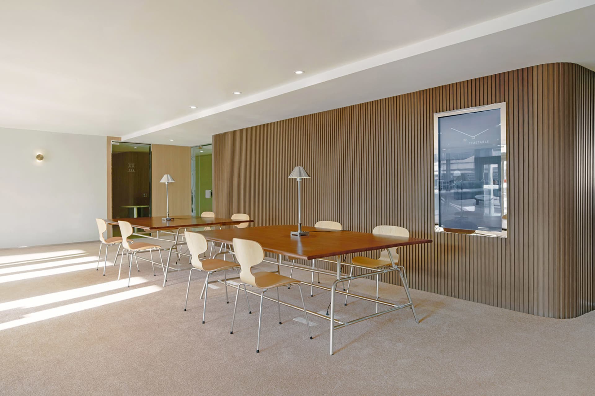 A professional office space with a large wooden dining table surrounded by multiple white chairs, creating a comfortable seating arrangement for collaboration and communication