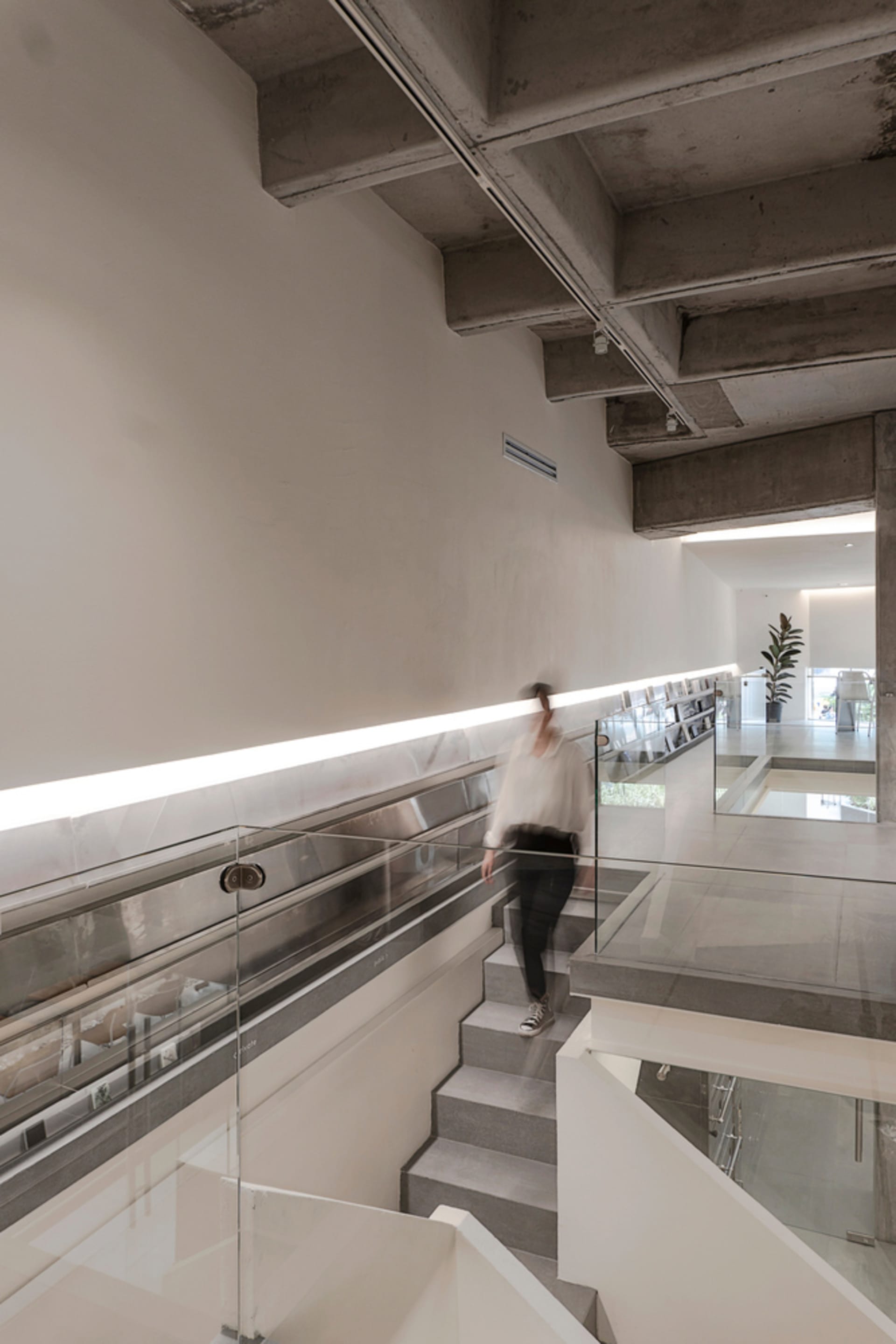A modern stairwell with concrete stairs and a glass railing, well-lit with natural and artificial light