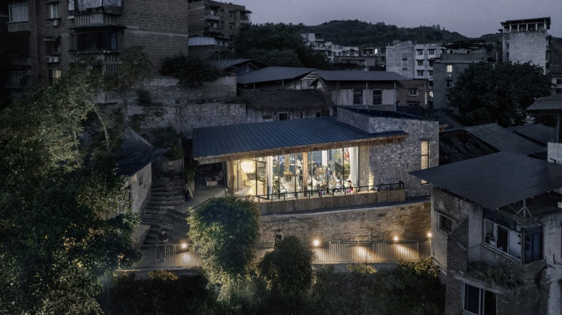 A rustic building with a stone exterior and a large patio area, featuring people gathered for a social event