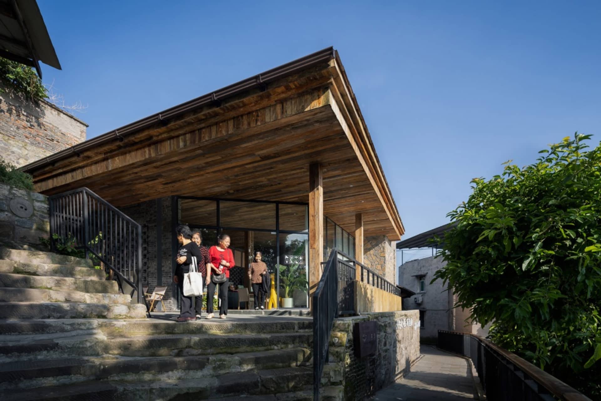 A group of people stand outside an old wooden building with a rustic charm, surrounded by natural surroundings