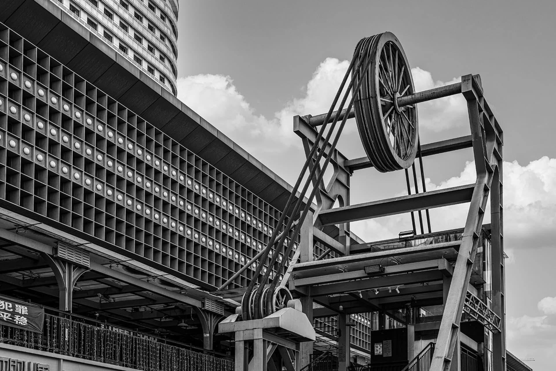 A building with a large metal structure in front of it, featuring many windows and a crane-like pulley system, suggesting a construction or renovation site