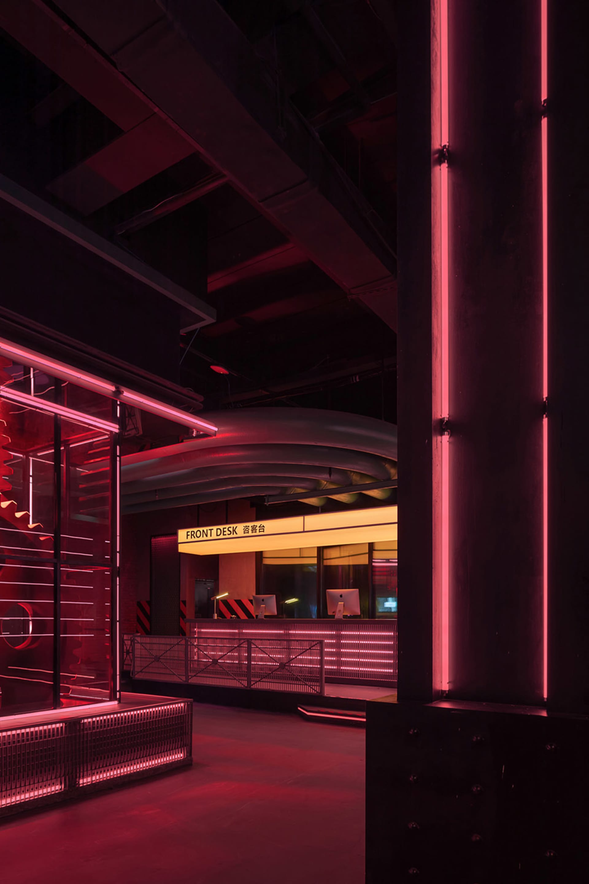 Office interior with two desks, chairs, and TV screens, surrounded by a red neon sign outside