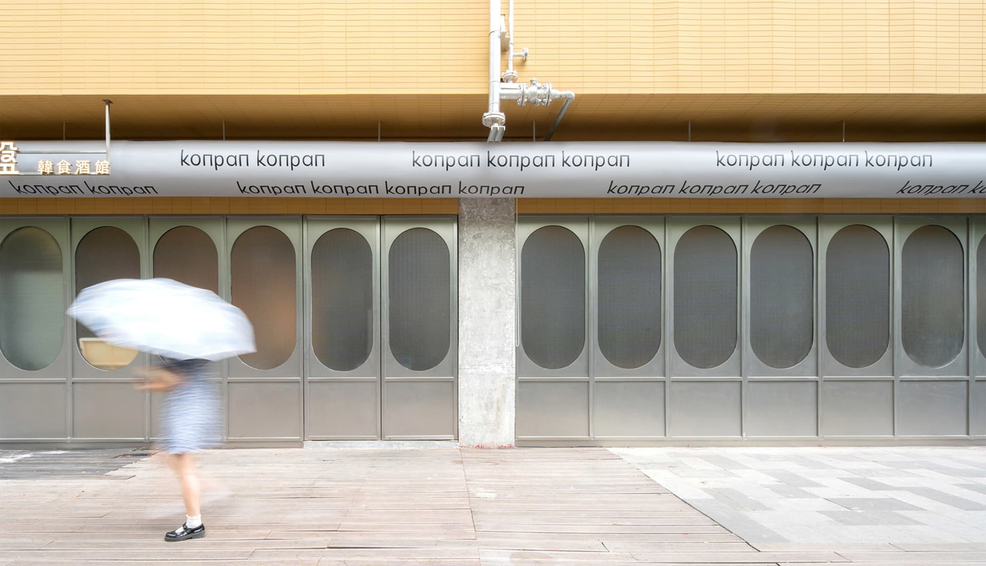 A commercial building with two large glass doors, one on either side, with the word Konpan written in white letters, made of concrete