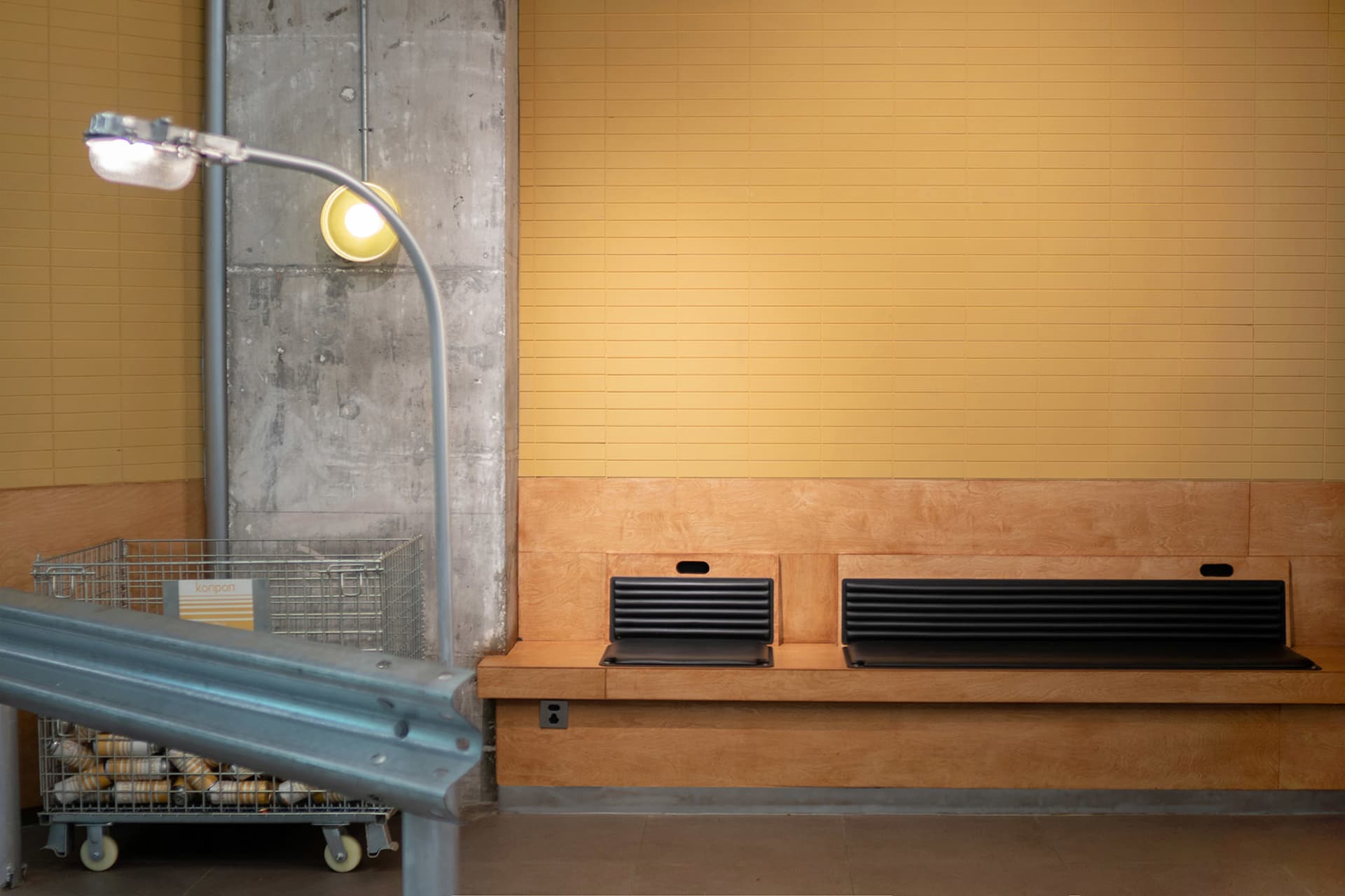 A casual interior space with two benches against a yellow wall, one with a black backrest, and two cups nearby