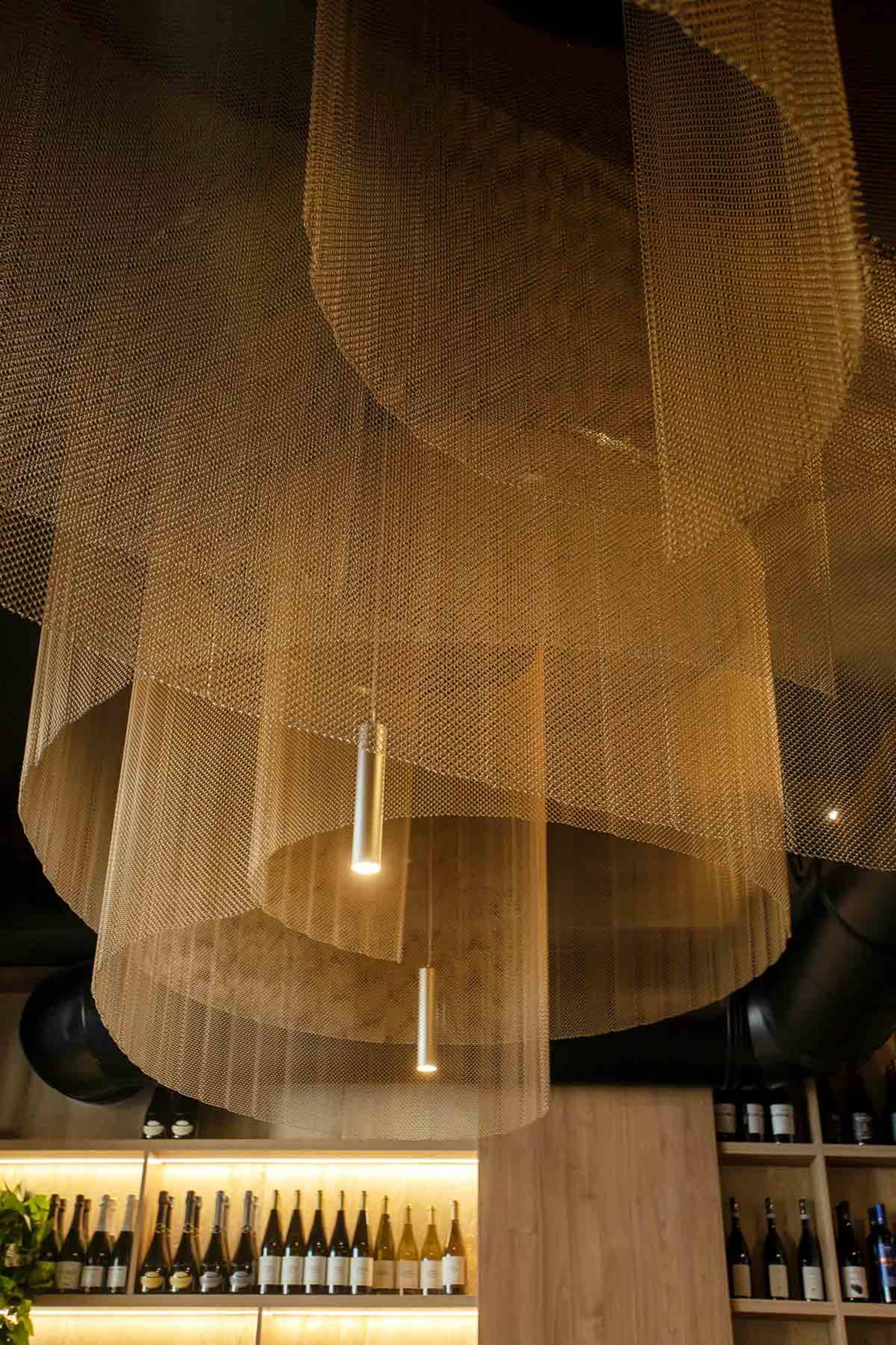 A dimly lit room with a minimalist aesthetic, featuring a large mesh ceiling fixture with suspended lights, creating a cozy atmosphere
