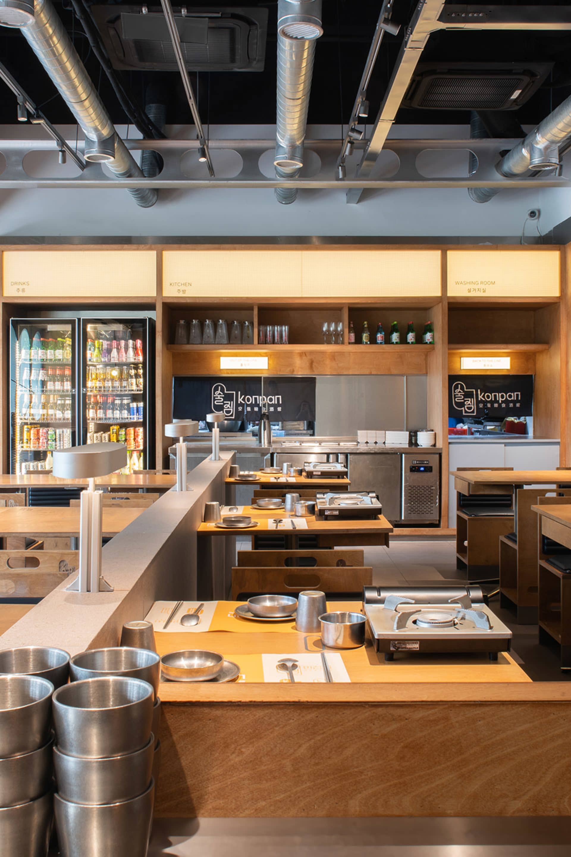 A commercial kitchen with wooden floors and cabinets, featuring multiple appliances, sinks, and ovens, with various bottles and ingredients visible