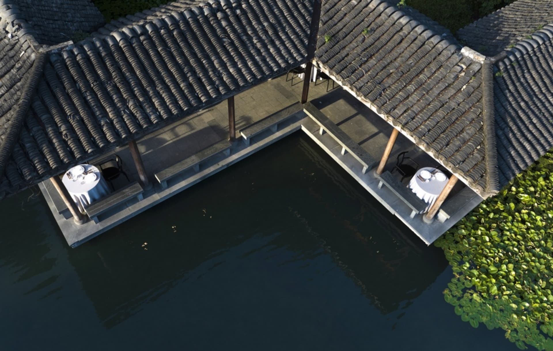 Two Asian-style houses with a wooden exterior, surrounded by greenery, and a water feature with a bridge between them
