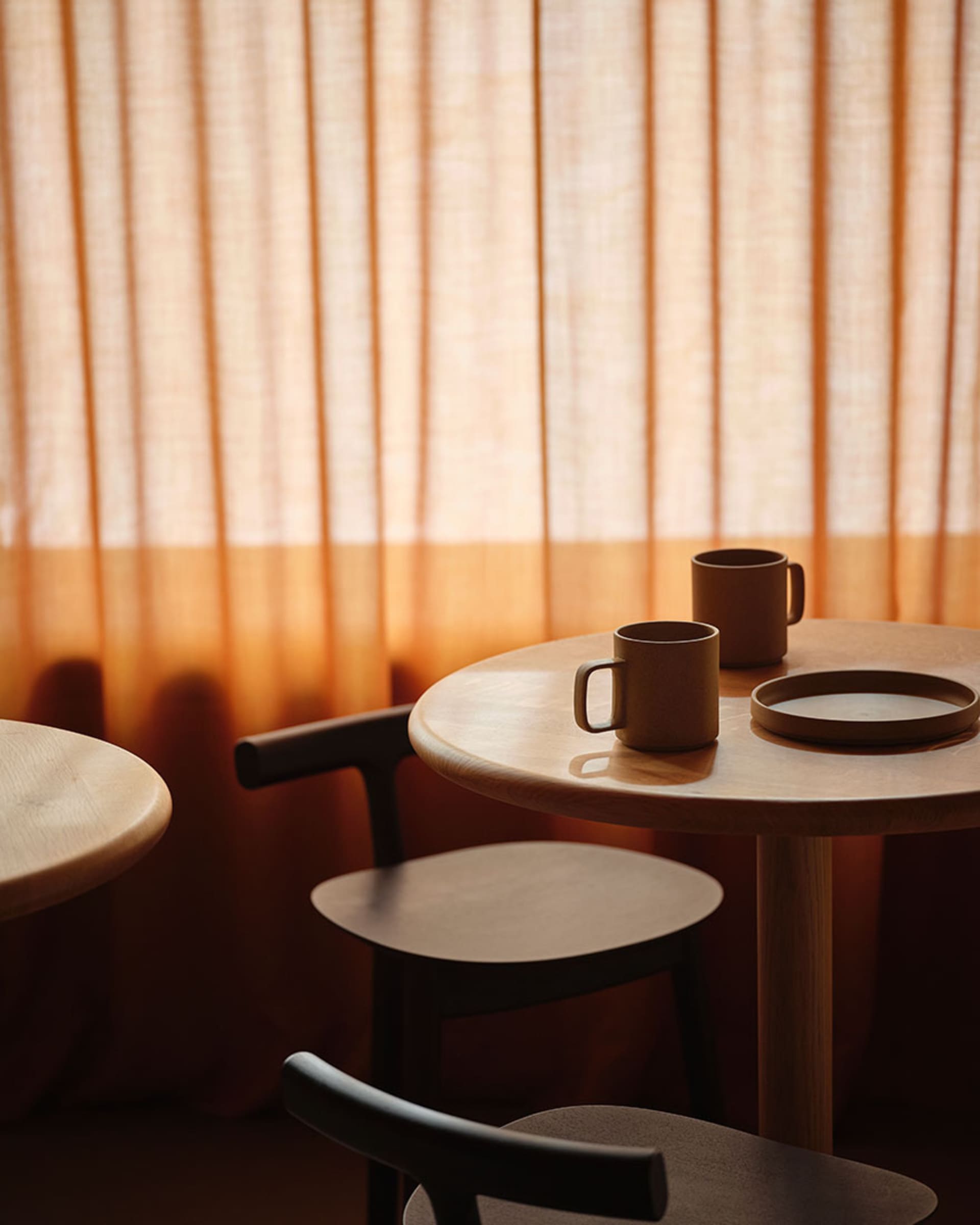 A warm and inviting dining space with two wooden tables, chairs, and a bowl and coffee cups, set up for a meal or gathering