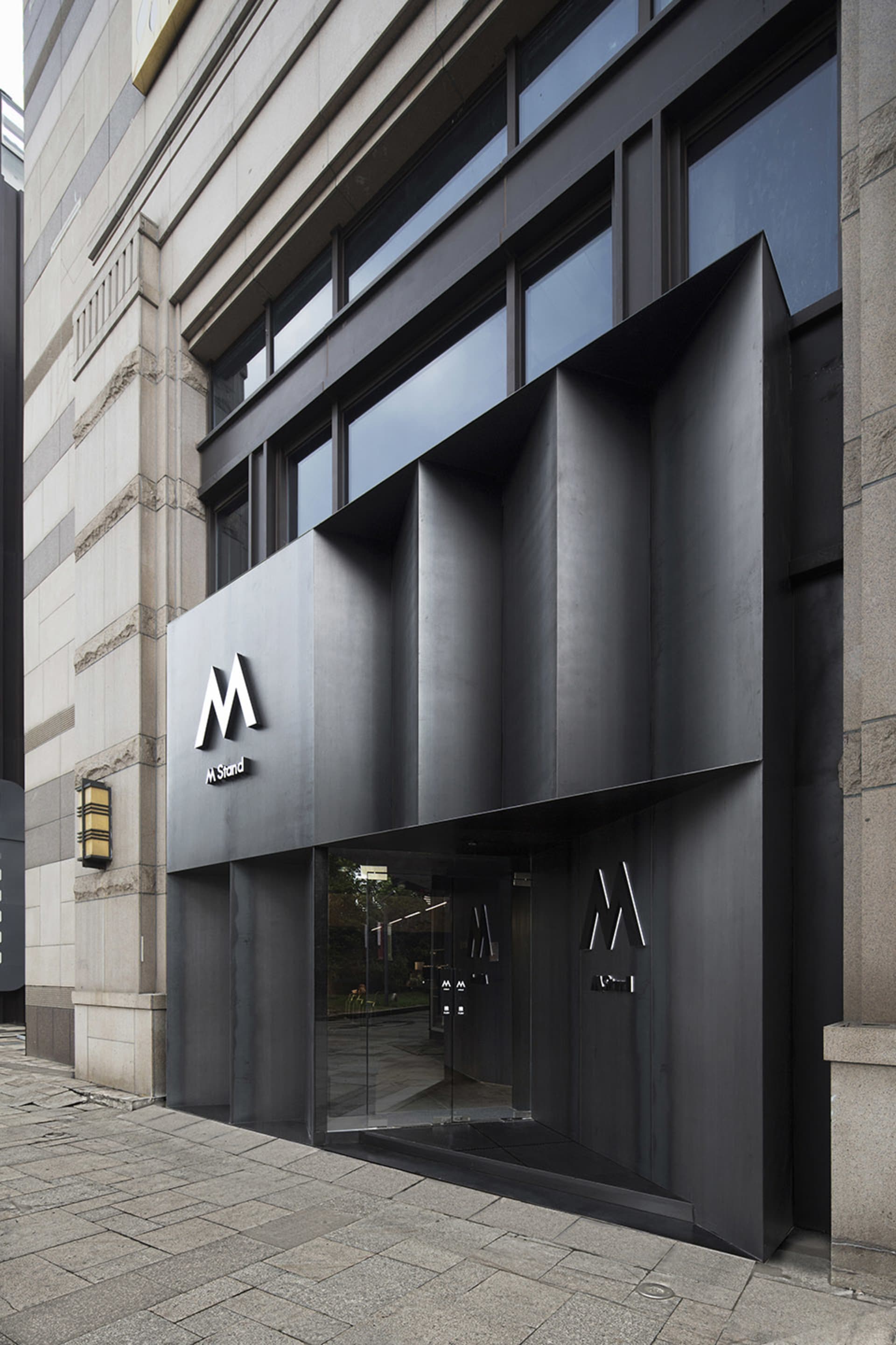 Modern lobby entrance with a glass door, metal frame, and potted plants, featuring clean lines and minimalistic design elements